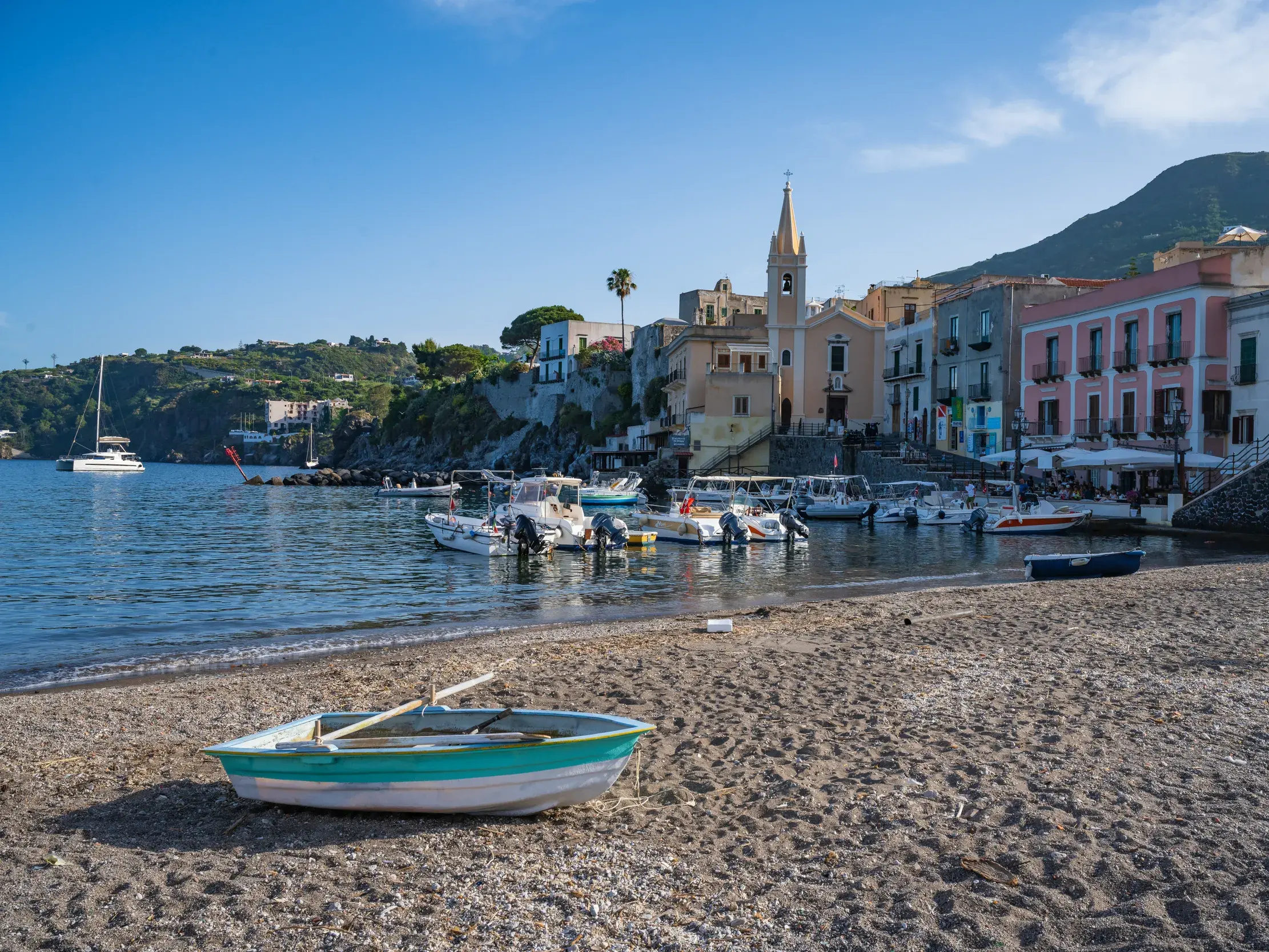 Ein Boot liegt am Strand im Hafen von Lipari, dahinter die bunten Häuser und der Kirchturm der Stadt auf den Äolischen Inseln.