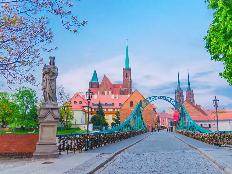 Steinerne Statuen flankieren den Weg über eine Brücke zur historischen Dominsel von Breslau an einem sonnigen Tag.
