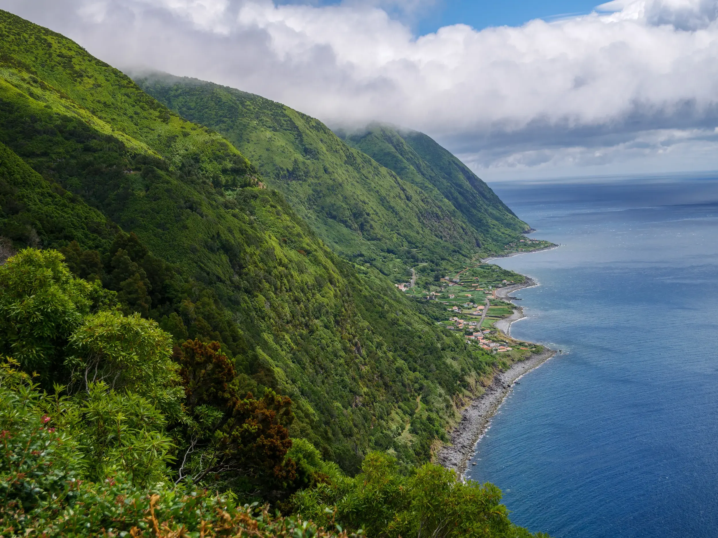 Spektakulärer Ausblick beim Wandern auf der Azoreninsel São Jorge: Die grüne Steilküste trifft auf eine fruchtbare Fajã am Atlantik.
