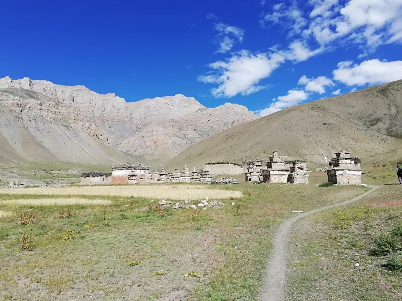 Eine Reihe steinerner Chörten säumt einen Wanderpfad im weiten, kargen Tal von Dolpo, umgeben von Nepals Bergwelt.