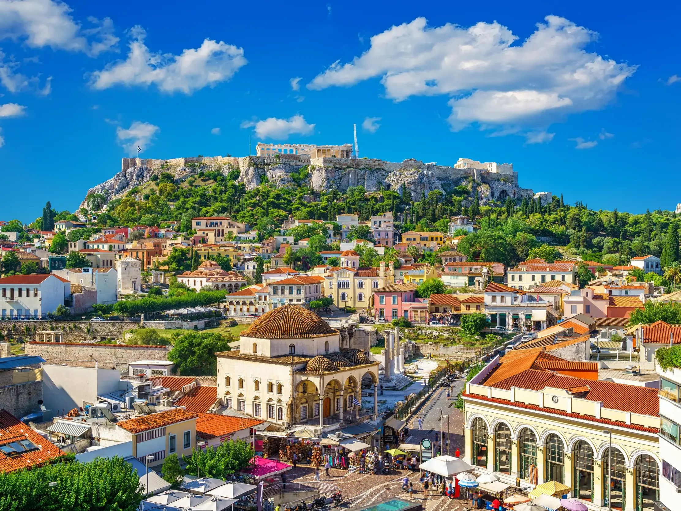 Die historische Akropolis thront über den Dächern und belebten Gassen der Altstadt Plaka in Athen an einem sonnigen Tag.