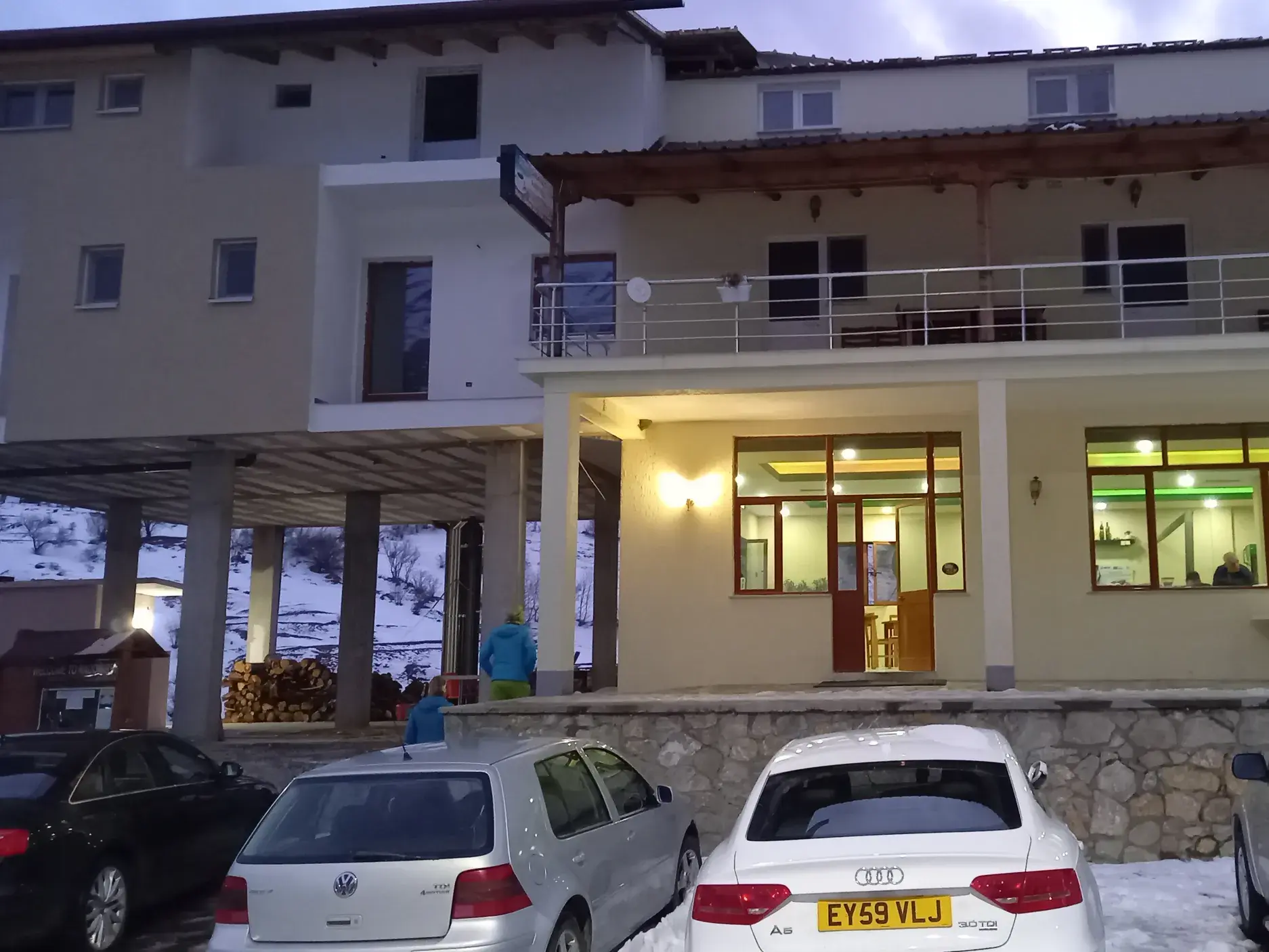 Abendliche Außenansicht einer landestypischen Pension im Balkan für Skitouren, umgeben von Schnee mit erleuchteten Fenstern.