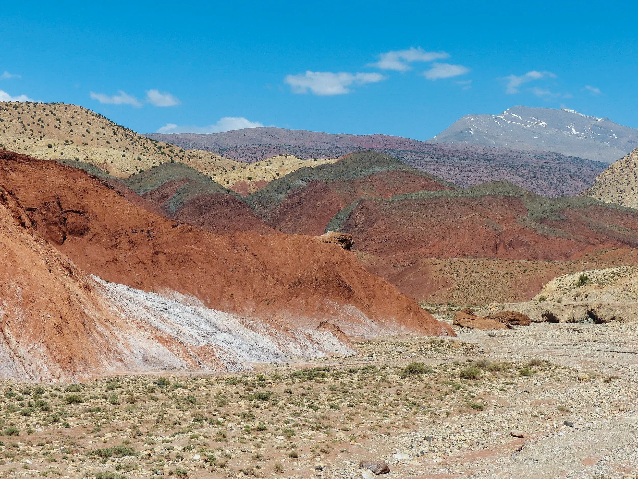 Karge Tallandschaft beim Trekking im Hohen Atlas mit leuchtend roten Felsformationen und einem hohen Gipfel im Hintergrund.