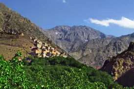 Sonnenbeschienenes Berberdorf an einem Berghang im Hohen Atlas vor der Kulisse des schneebedeckten Djebel Toubkal.