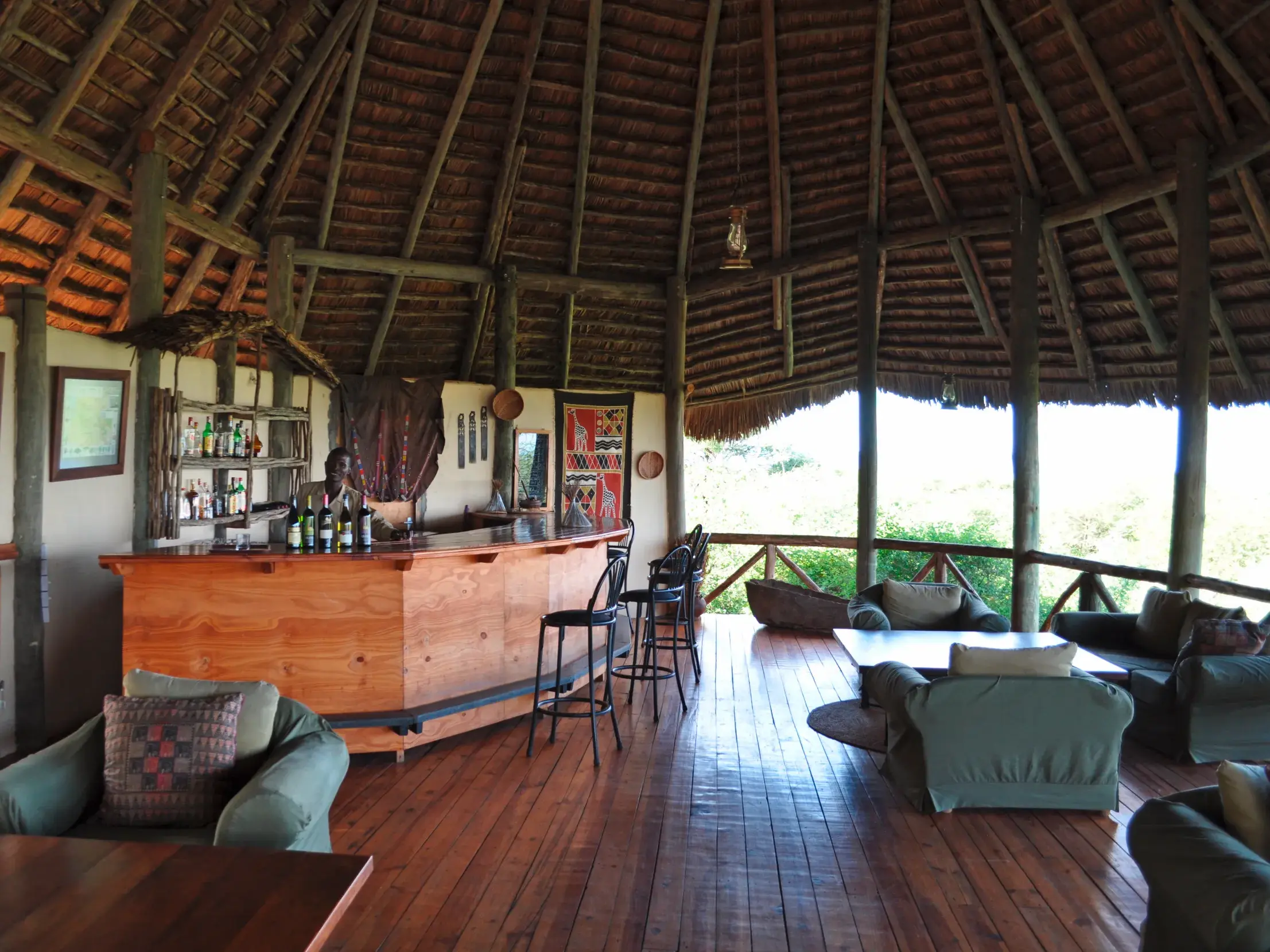 Rustikale Bar einer Safari-Lodge in Tansania mit Holztresen, Strohdach und gemütlichem, offenem Loungebereich.