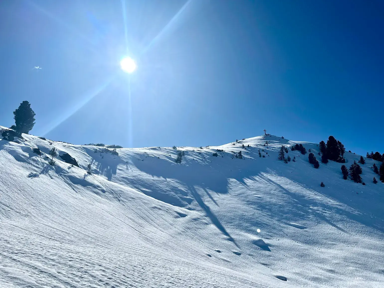 Unberührter Schneehang führt zum Gipfelkreuz der Breiteggspitze in den Kitzbüheler Alpen bei strahlendem Sonnenschein.