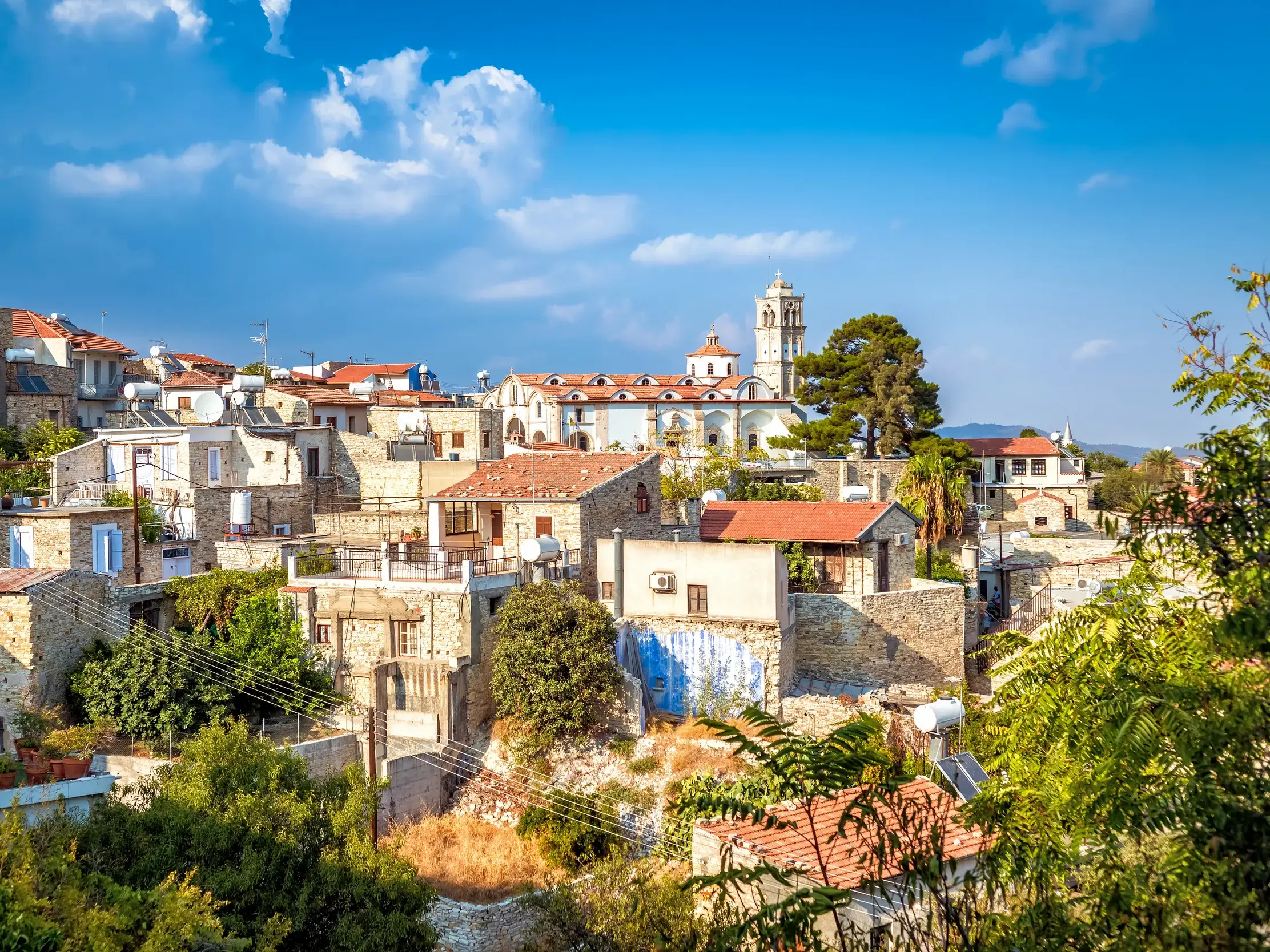 Malerischer Blick auf das Bergdorf Lefkara auf Zypern mit traditionellen Steinhäusern und einer Kirche unter blauem Himmel.