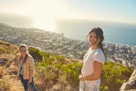 Zwei junge Frauen einer Gruppenreise genießen auf dem Signal Hill den sonnigen Panoramablick über Kapstadt und das Meer.