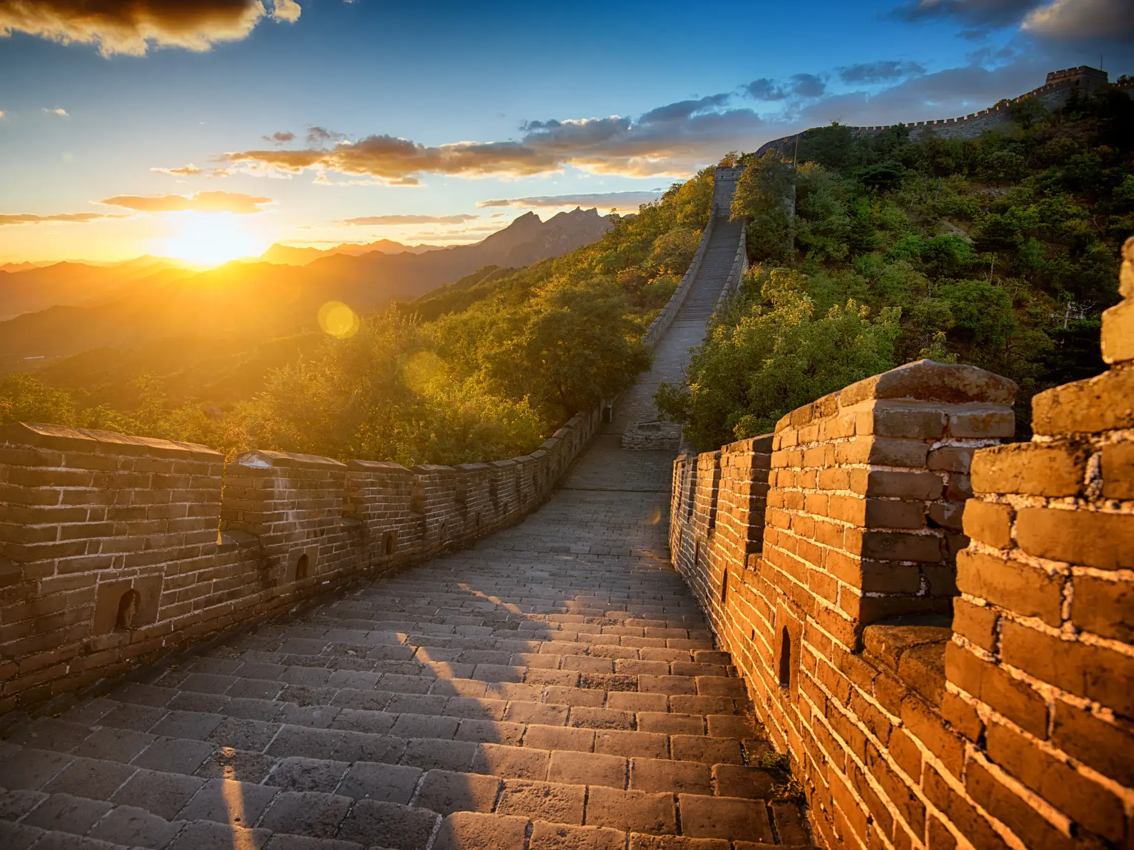 Atmosphärischer Sonnenuntergang an der Großen Mauer bei Simatai, deren steinerne Stufen sich über grüne Berge schlängeln.