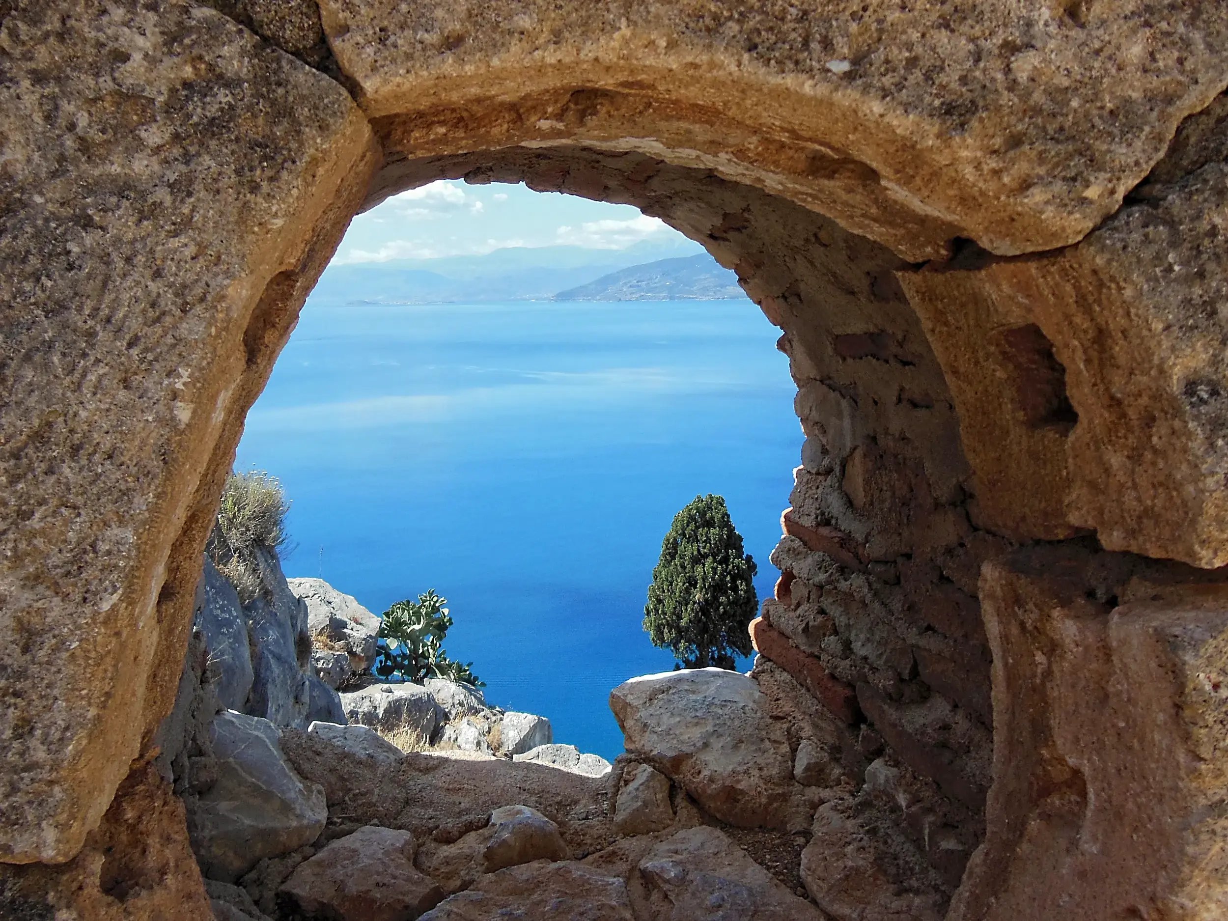 Panoramablick durch einen Steinbogen der Palamidi-Festung in Nauplia auf die tiefblaue Bucht von Argolis.