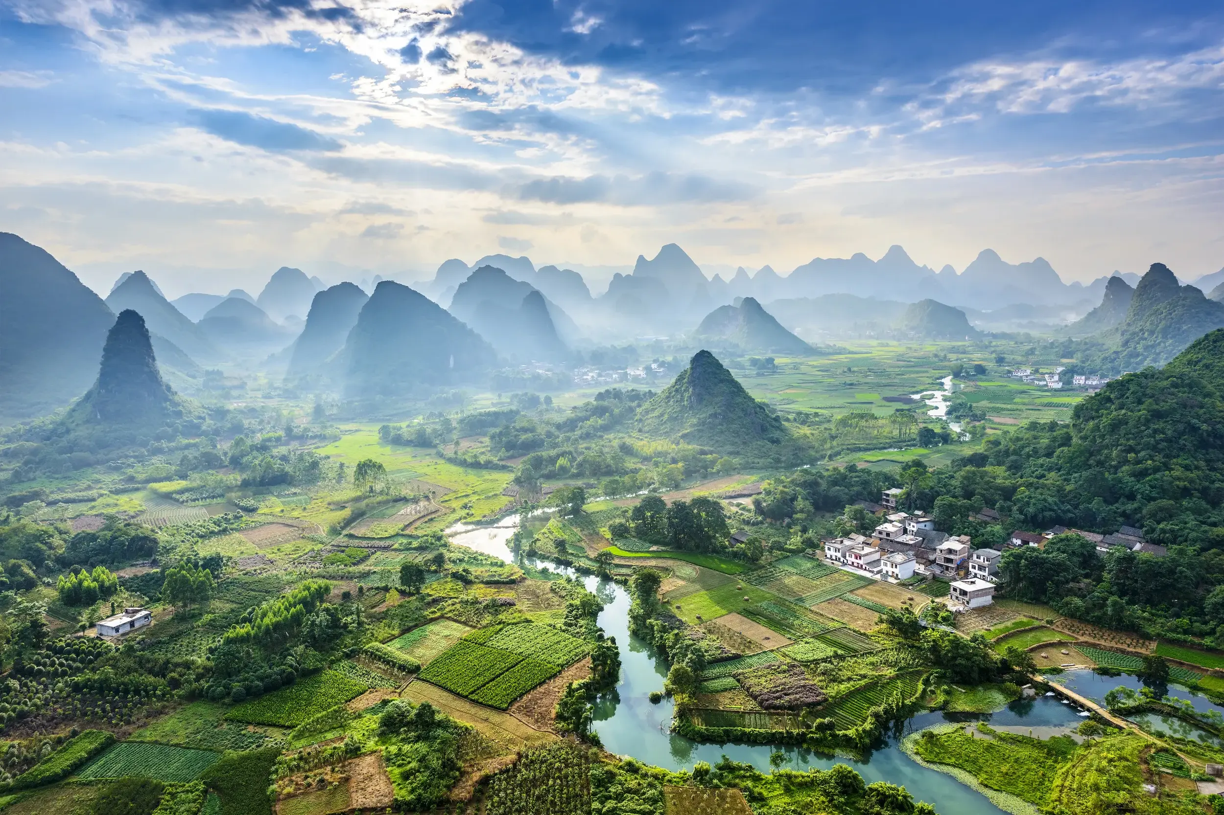 Weitblick von einem Aussichtsberg auf die spektakuläre Karstlandschaft von Yangshuo mit grünen Reisfeldern und Fluss.