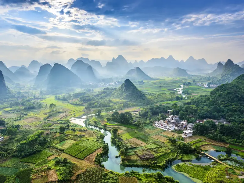 Weitblick von einem Aussichtsberg auf die spektakuläre Karstlandschaft von Yangshuo mit grünen Reisfeldern und Fluss.
