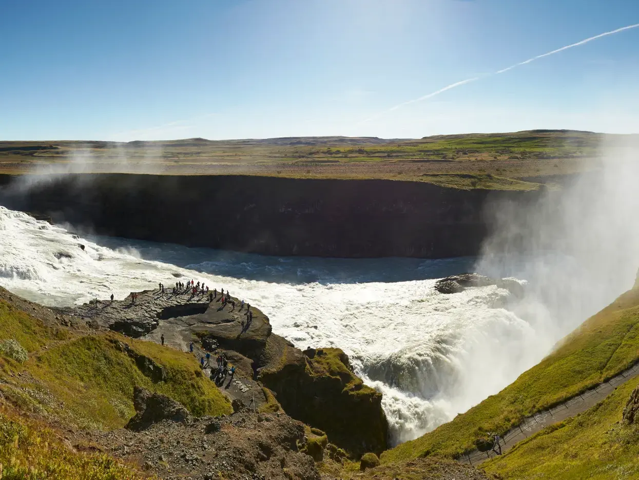Eine kleine Reisegruppe bestaunt an einem sonnigen Tag den mächtigen Gullfoss Wasserfall am Golden Circle in Island.