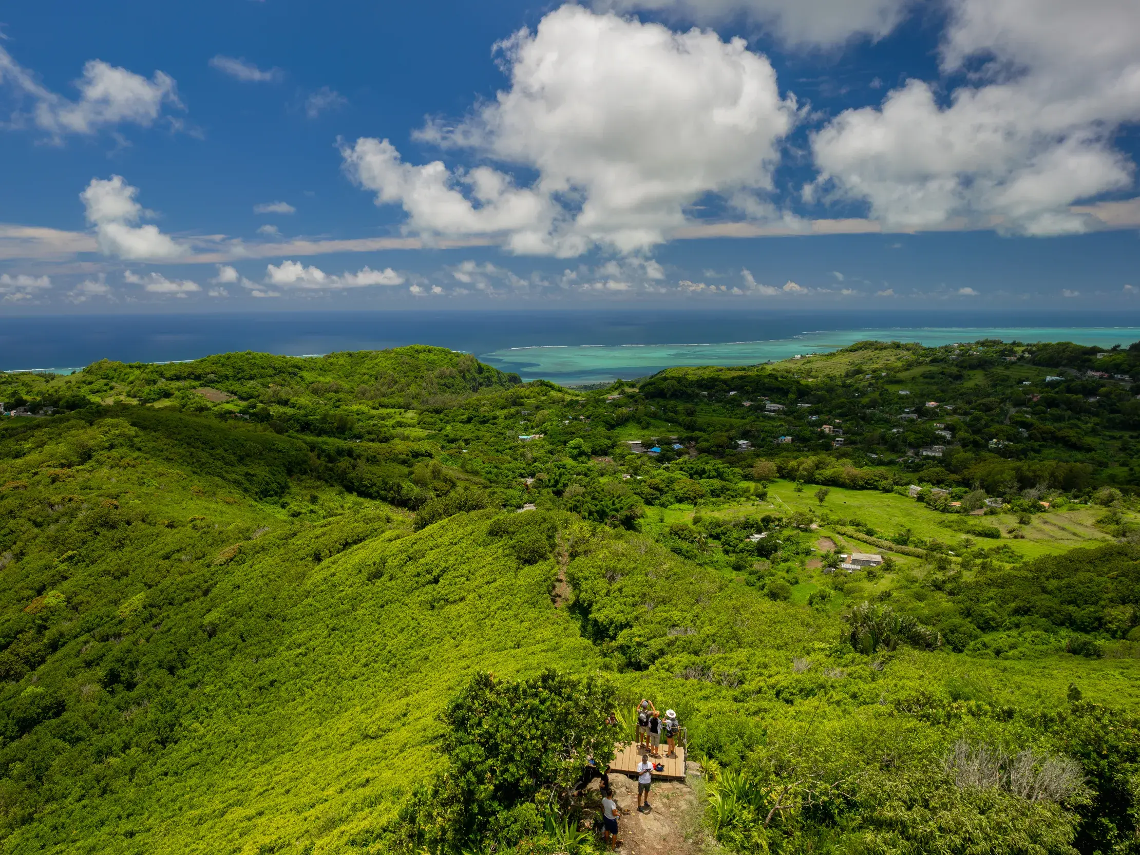 Kleine Reisegruppe auf einem Wanderweg vom Mont Limon auf Rodrigues mit Panoramablick über grüne Hügel zum Indischen Ozean.