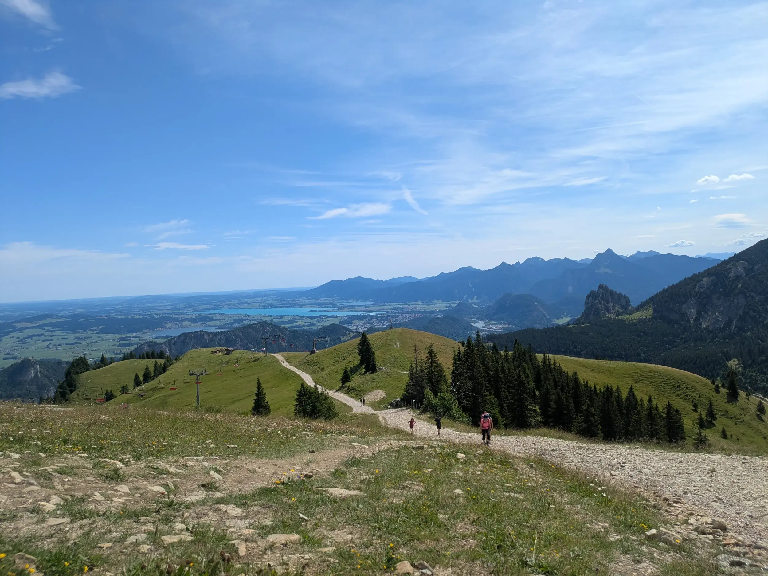Wandergruppe auf einem Panoramaweg in den Ammergauer Alpen mit Weitblick über das hügelige Ostallgäu und die Seen.