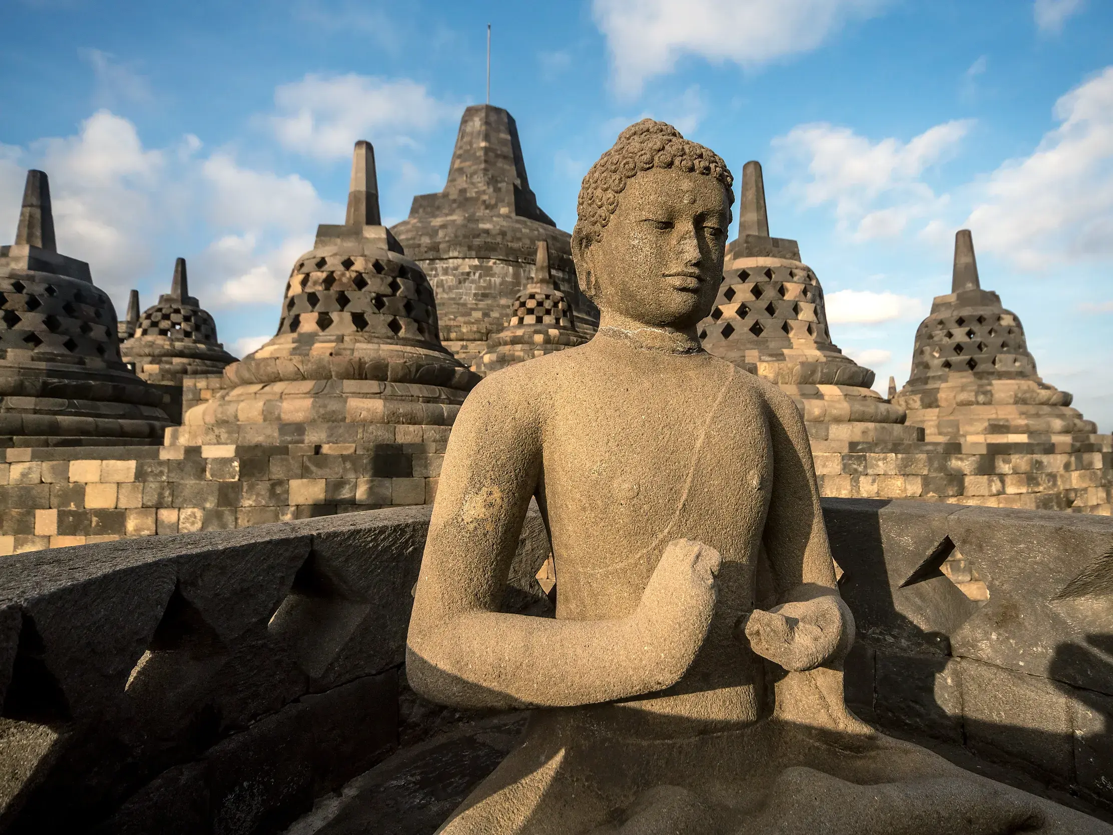 Eine steinerne Buddha-Statue in der UNESCO-Welterbestätte Borobudur auf Java, umgeben von glockenförmigen Stupas.