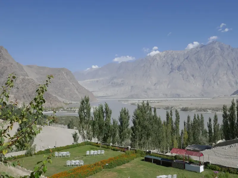 Ausblick von einer grünen Hotelterrasse in Skardu über das weite Tal des Indus auf die imposante Bergkette des Karakorum.