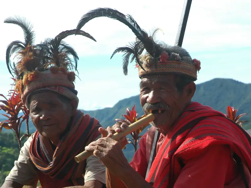 Kulturelle Begegnung auf Luzon: Ein Einheimischer spielt auf einer Bambusflöte, beide tragen traditionellen Federschmuck.