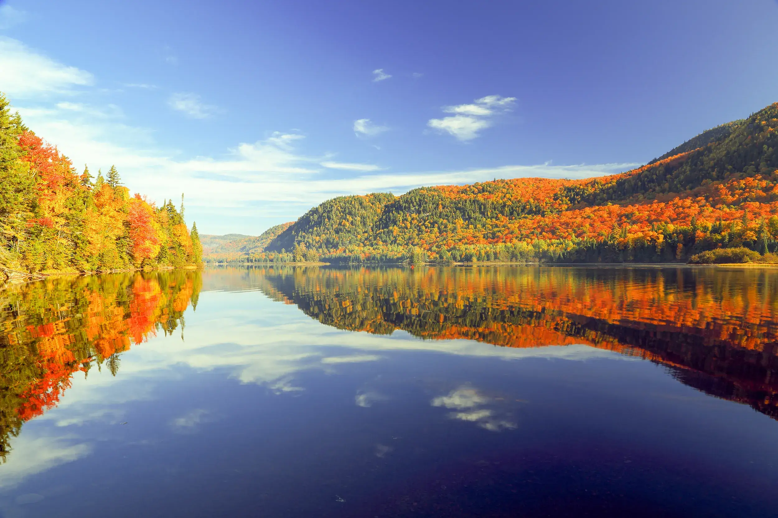 Indian Summer in Québec: Bunte Wälder und ein blauer Himmel spiegeln sich auf einem See im Jacques-Cartier-Nationalpark.