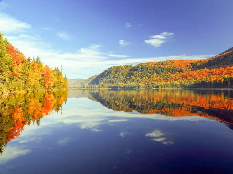 Indian Summer in Québec: Bunte Wälder und ein blauer Himmel spiegeln sich auf einem See im Jacques-Cartier-Nationalpark.