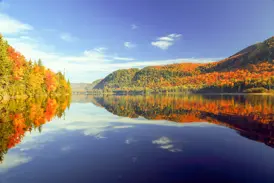 Indian Summer in Québec: Bunte Wälder und ein blauer Himmel spiegeln sich auf einem See im Jacques-Cartier-Nationalpark.