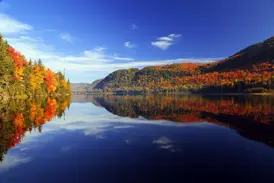 Farbenprächtiger Herbstwald im Indian Summer spiegelt sich im stillen Wasser eines Sees in einem Nationalpark in Québec.