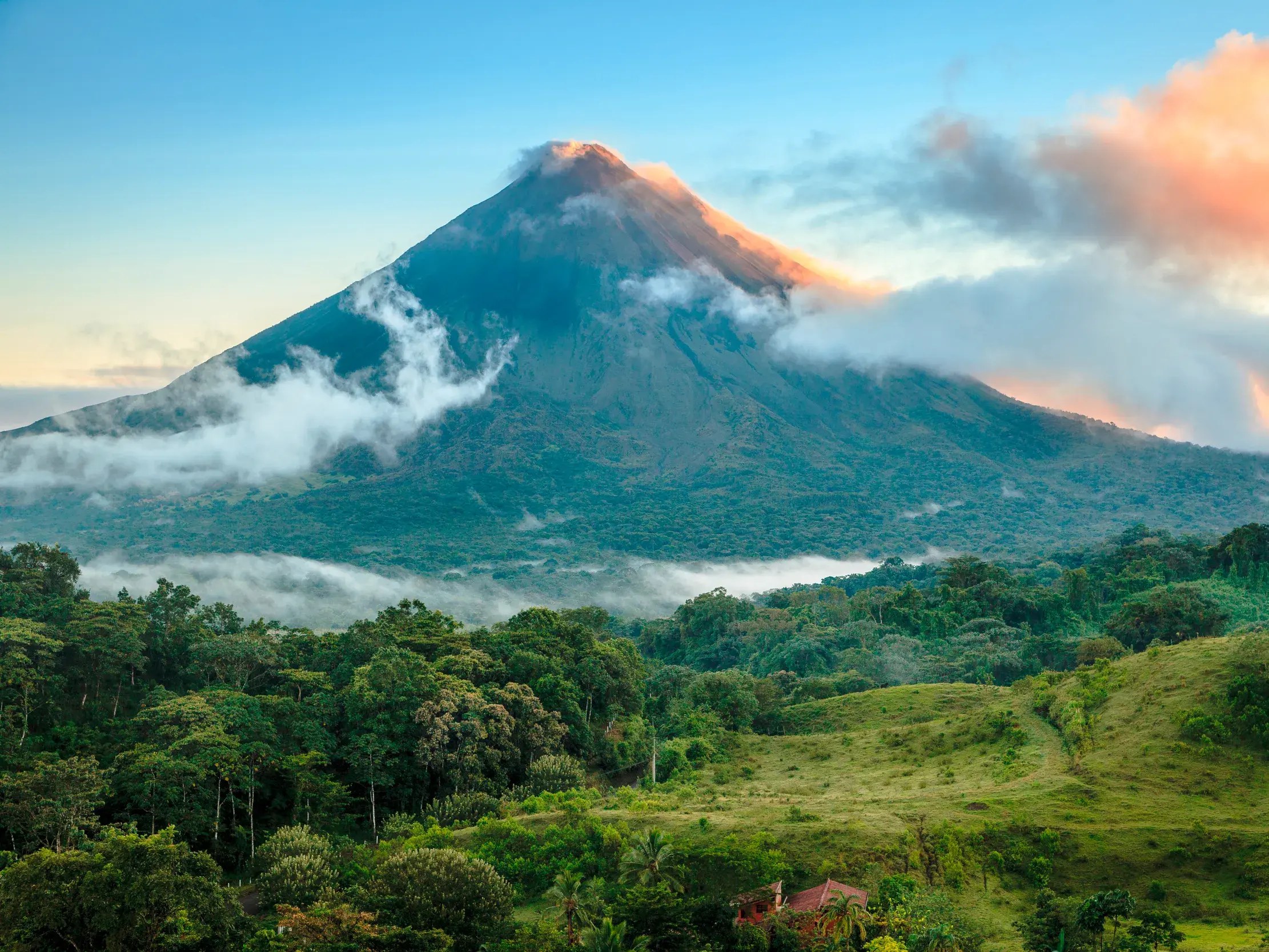 Der majestätische Vulkan Arenal in Costa Rica, dessen Gipfel von Wolken im Morgenlicht umspielt wird, über grünen Regenwäldern.