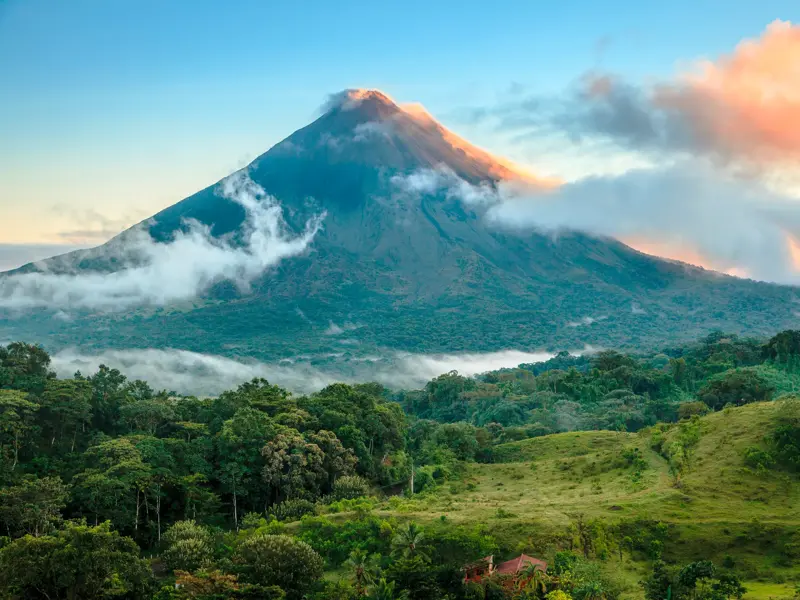 Der majestätische Vulkan Arenal in Costa Rica, dessen Gipfel von Wolken im Morgenlicht umspielt wird, über grünen Regenwäldern.