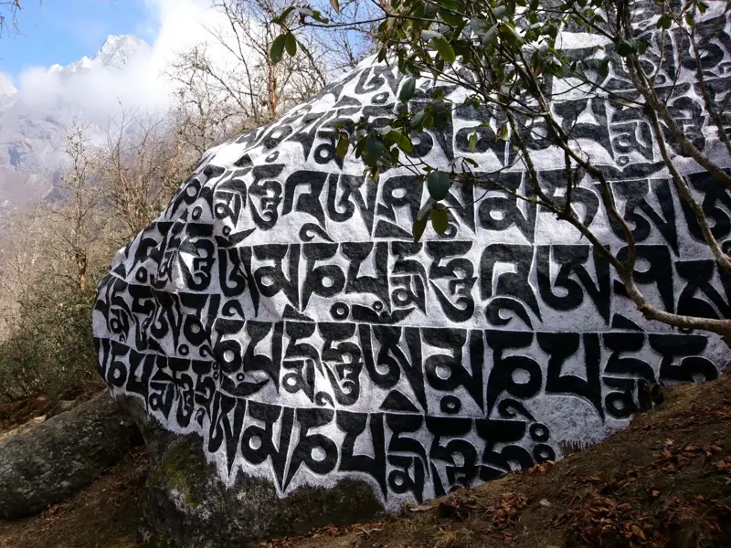 Großer Mani-Stein mit dem Mantra 'Om mani padme hum' am Trekkingpfad in der Everest-Region vor schneebedeckten Gipfeln.