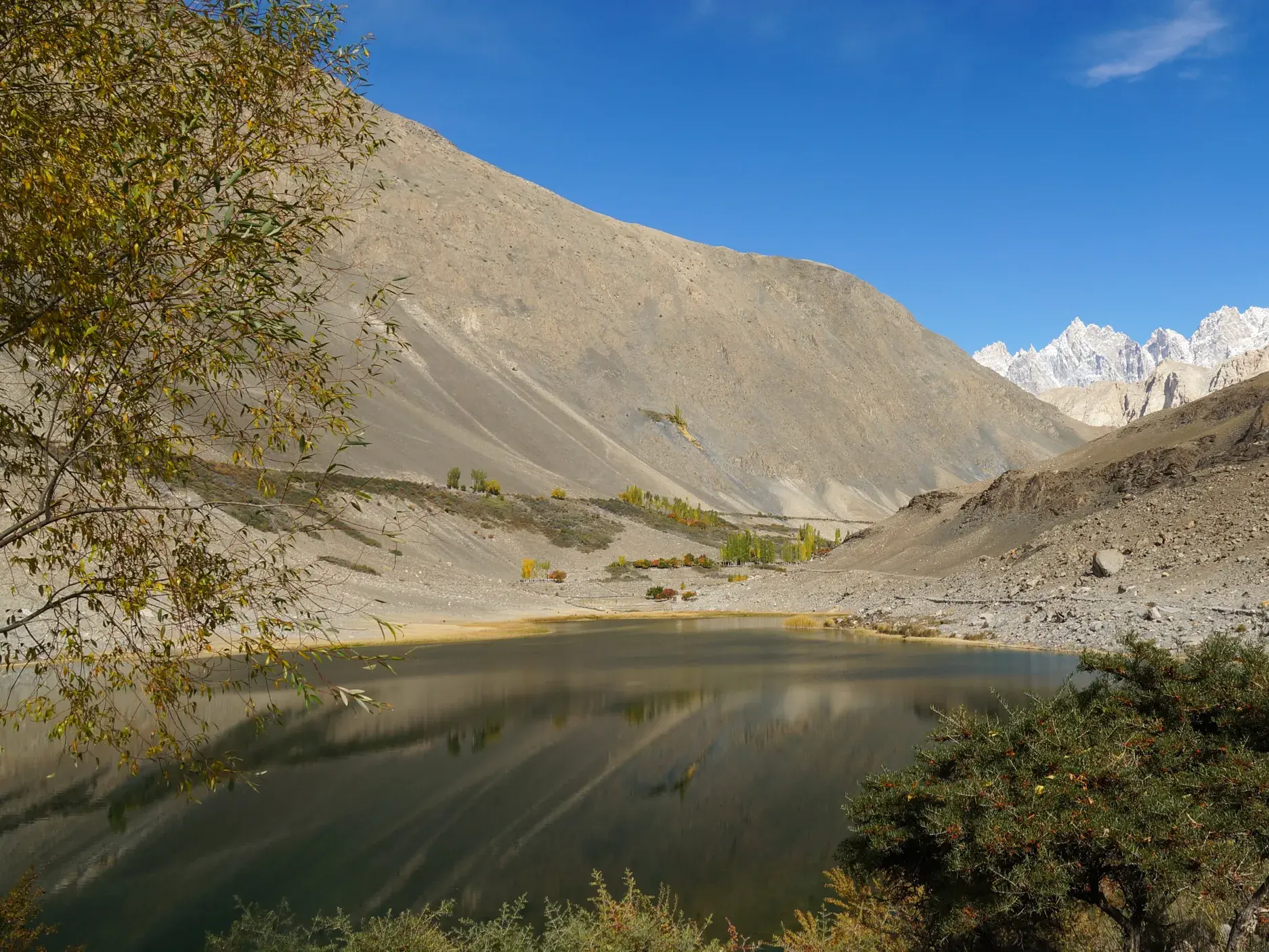 Der ruhige Borith-See im Hunza-Tal in Pakistan, umgeben von kargen Hängen mit Blick auf die schneebedeckten Passu-Gipfel.