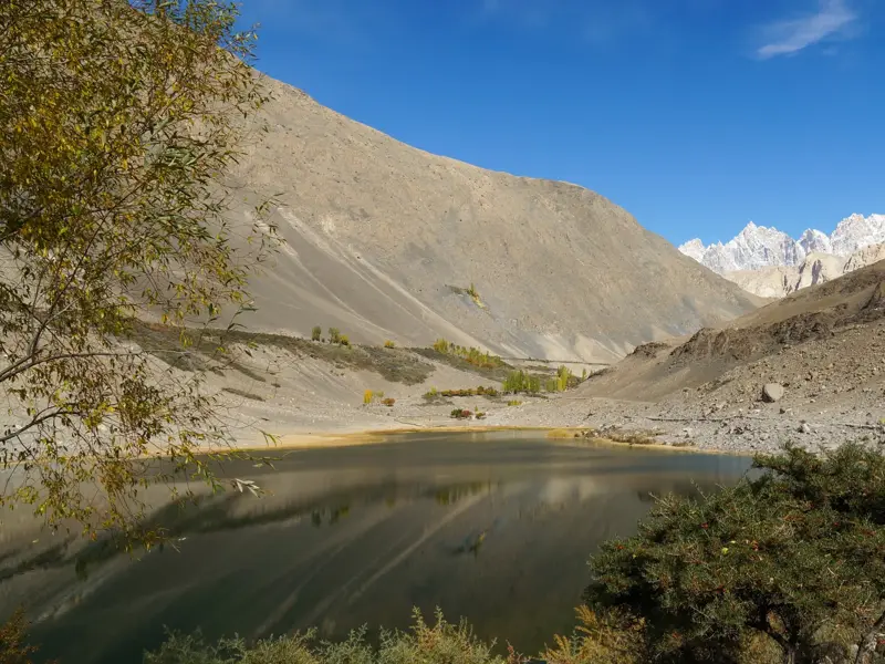 Der ruhige Borith-See im Hunza-Tal in Pakistan, umgeben von kargen Hängen mit Blick auf die schneebedeckten Passu-Gipfel.