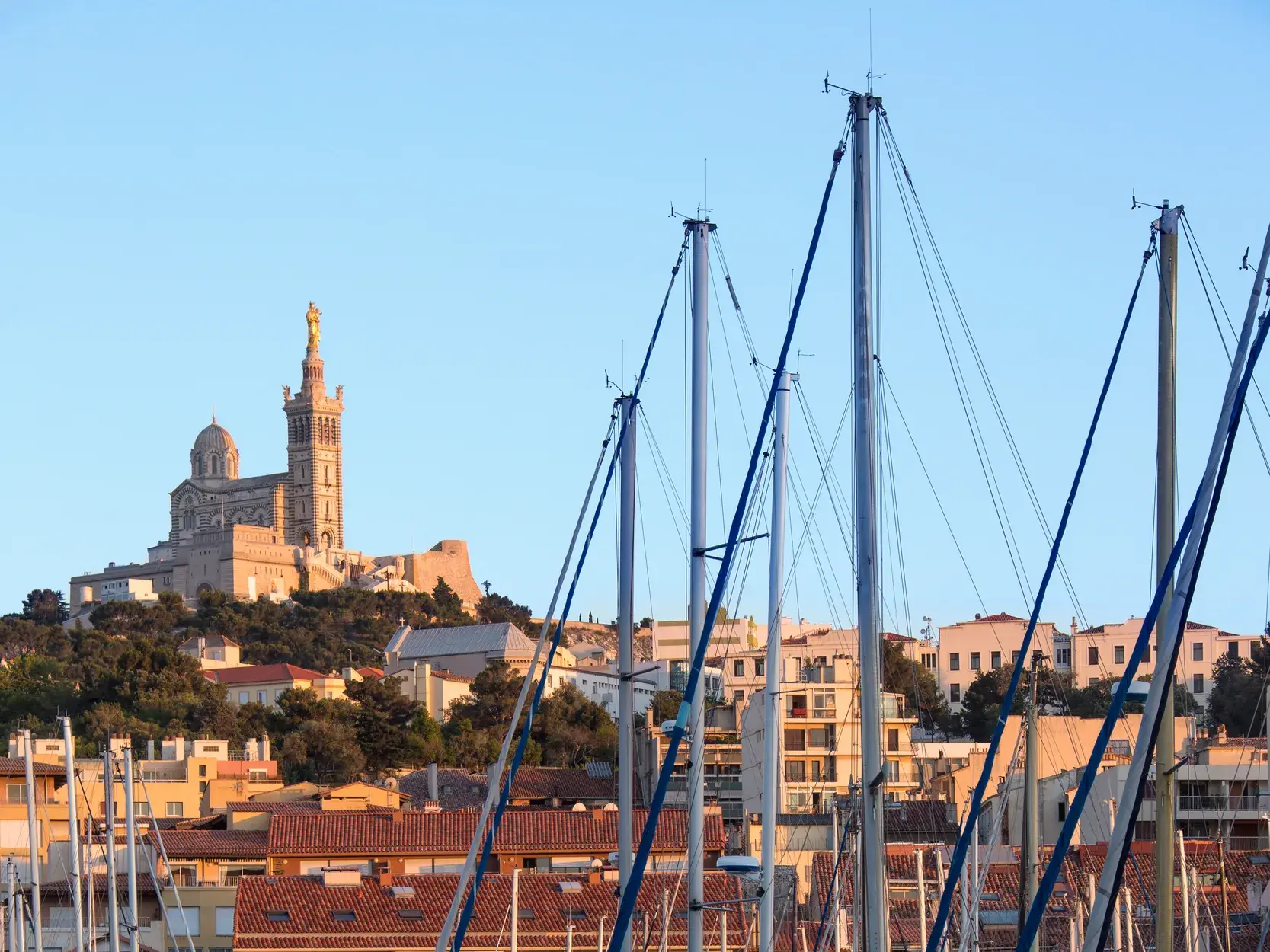 Blick über Segelbootmasten im Hafen von Marseille auf die Basilika Notre-Dame de la Garde.