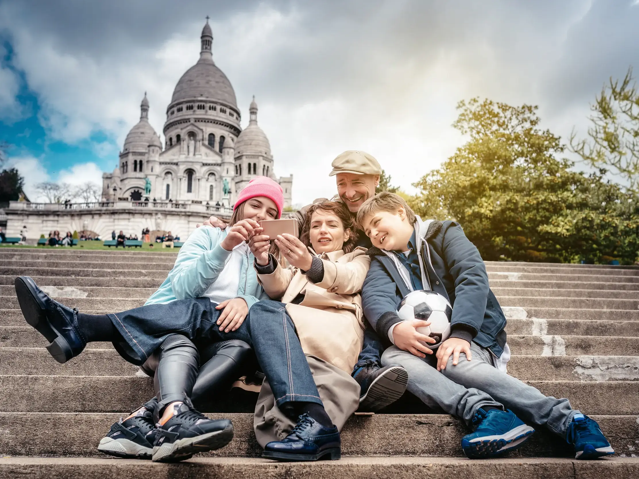 Eine fröhliche Familie sitzt während der Studiosus family Reise auf den Stufen vor Sacré Coeur auf dem Montmartre.