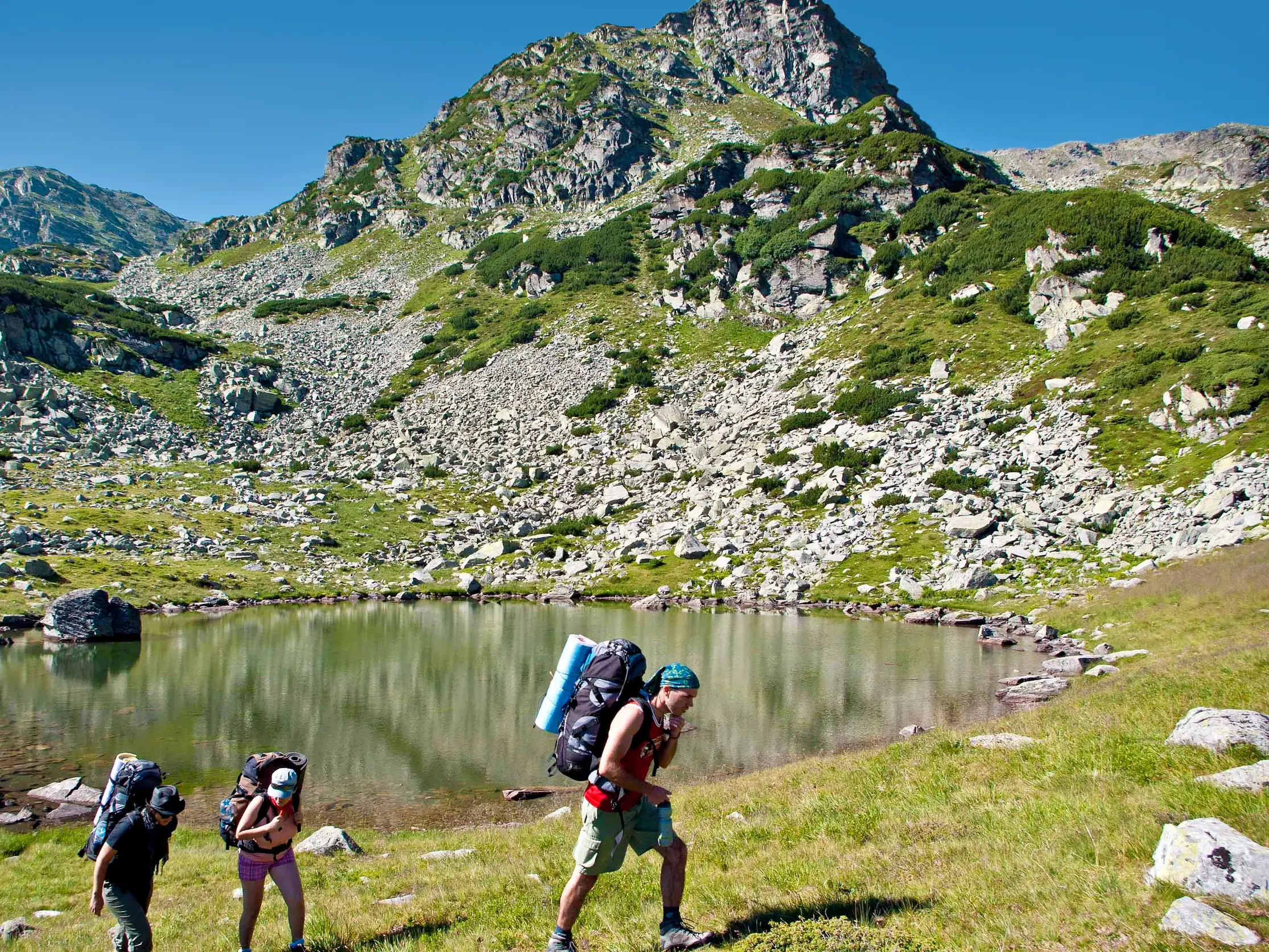 Eine kleine Trekking-Gruppe mit großen Rucksäcken steigt an einem Bergsee im rumänischen Fagaras-Gebirge auf.