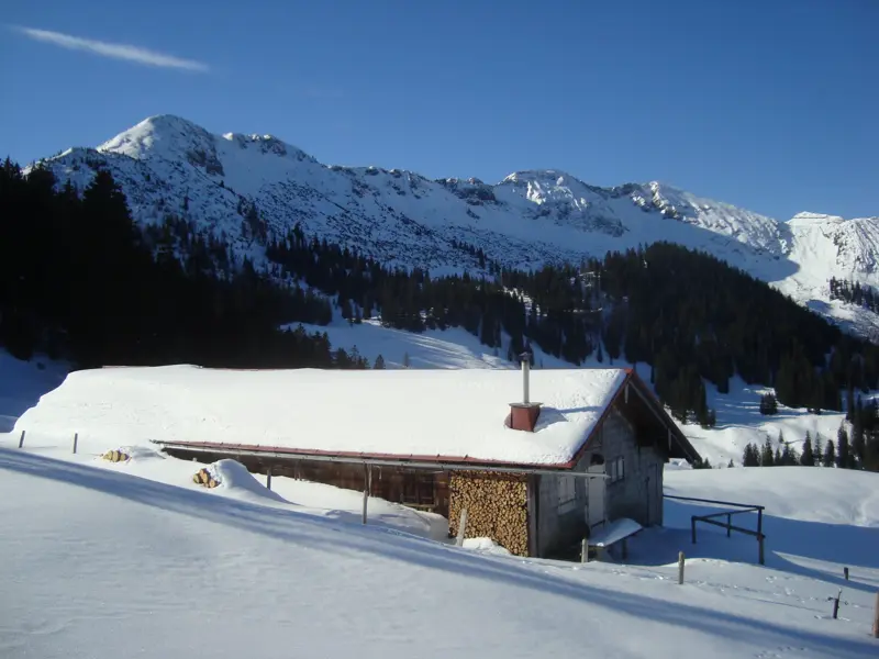 Tief verschneite Rontalalm vor der Nördlichen Karwendelkette im Karwendel an einem sonnigen Wintertag bei einer Wanderung.