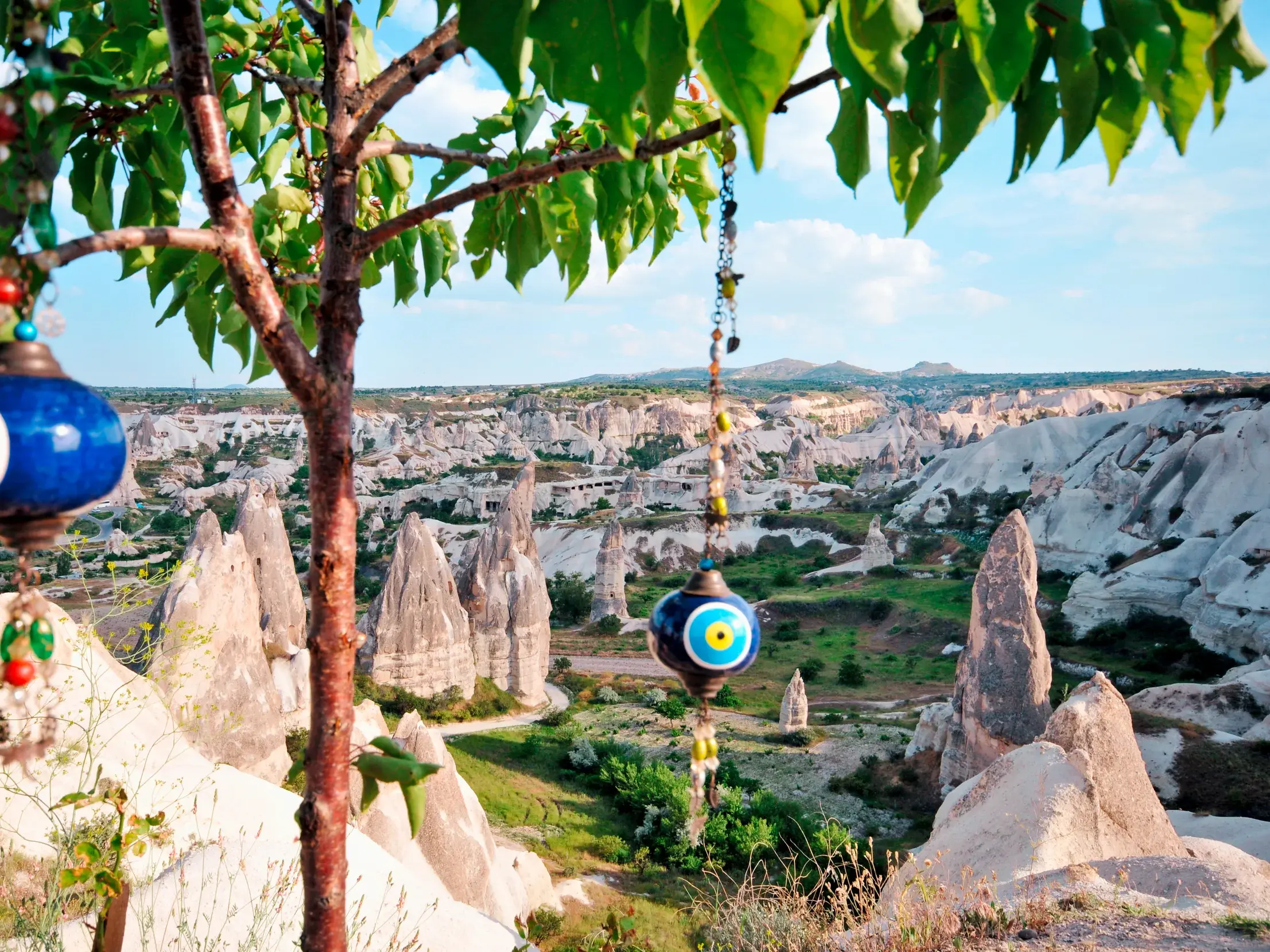 Blaue Nazar-Amulette an einem Baumzweig mit Blick auf die bizarre Felslandschaft der Feenkamine in Kappadokien.