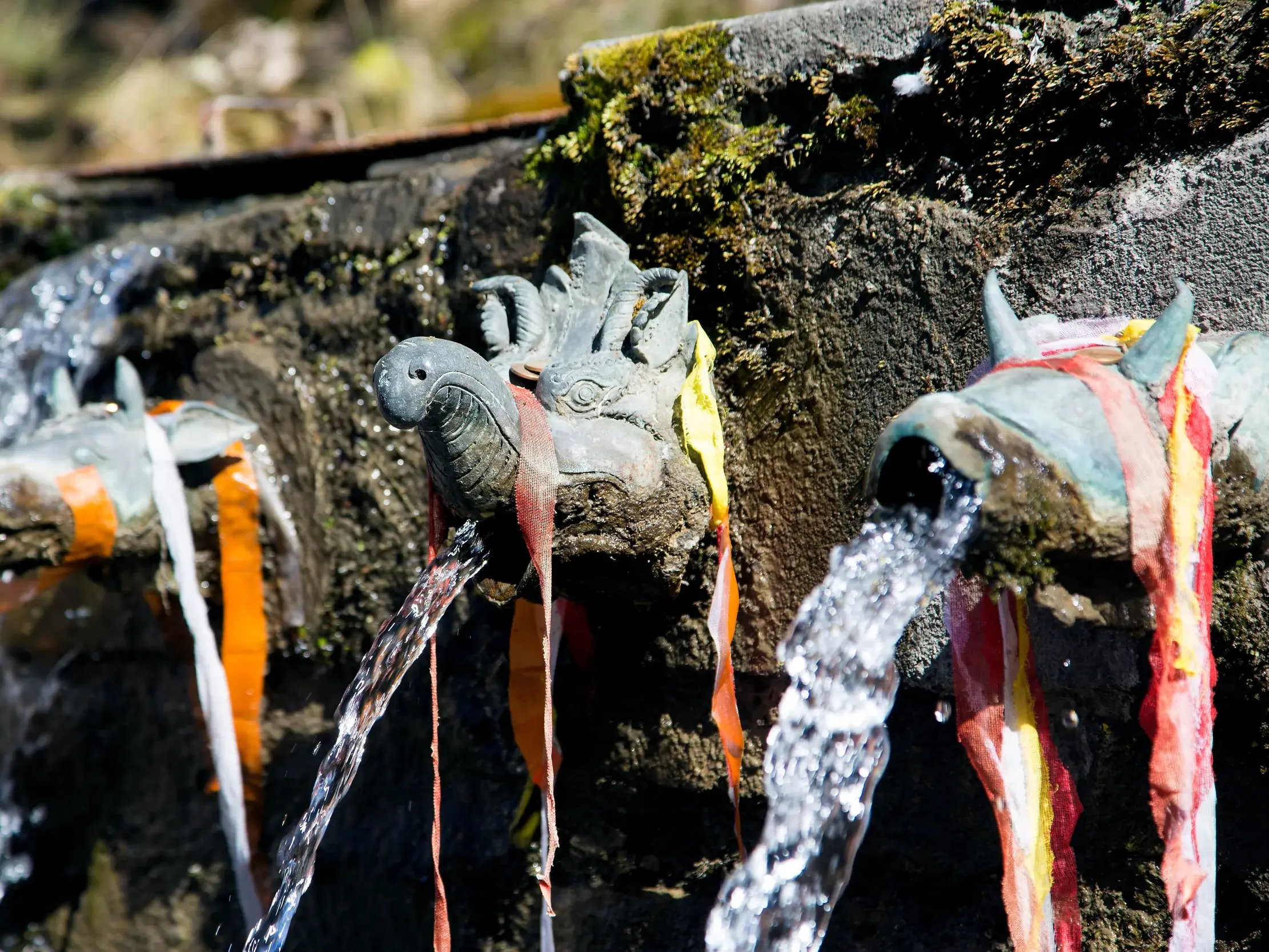 Klares Wasser strömt aus drei bronzenen, mit Gebetsbändern geschmückten Wasserspeiern am Pilgerort Muktinath in Nepal.
