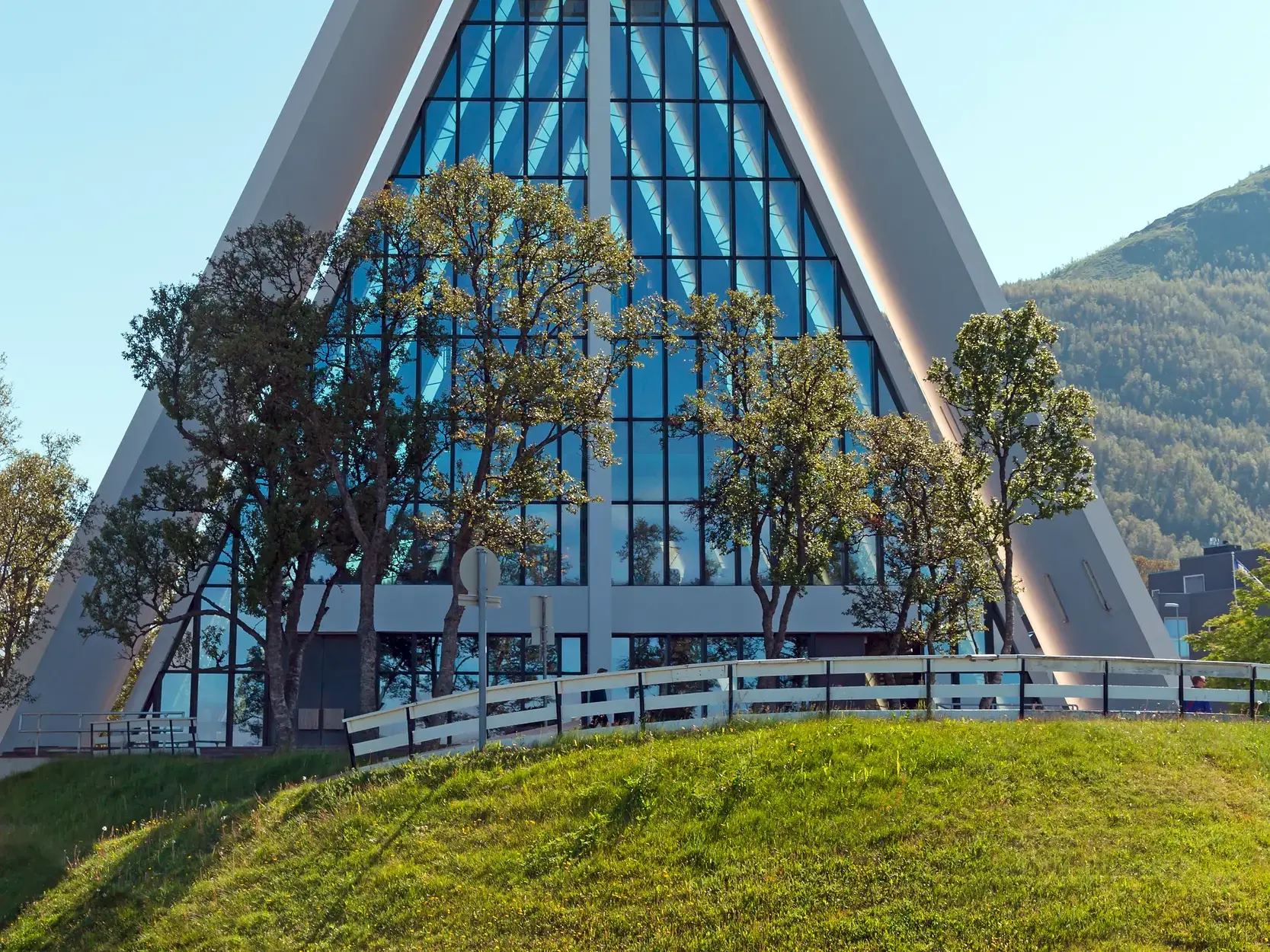 Die moderne Eismeerkathedrale in Tromsö mit ihrer markanten, dreieckigen Form und Glasfassade an einem sonnigen Sommertag.