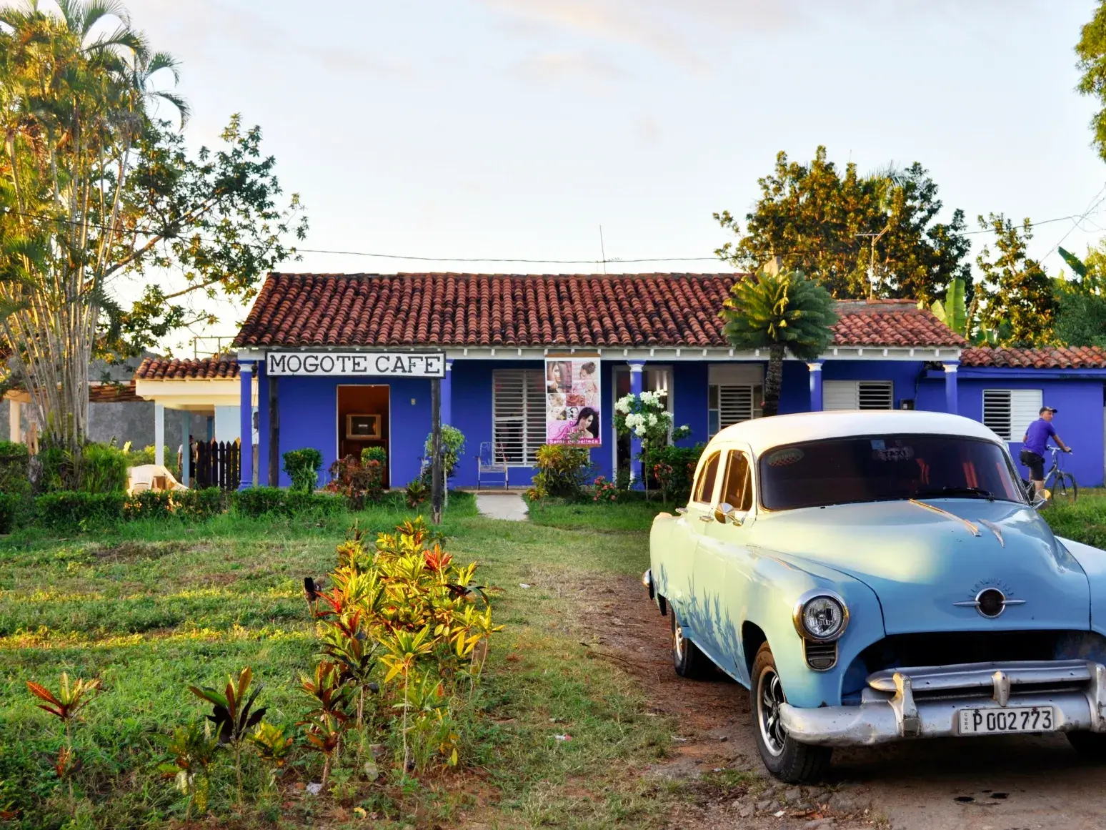 Hellblauer Oldtimer parkt auf einem Feldweg vor dem blauen Mogote Cafe im ländlichen Viñales-Tal auf einer Kuba Wanderreise.