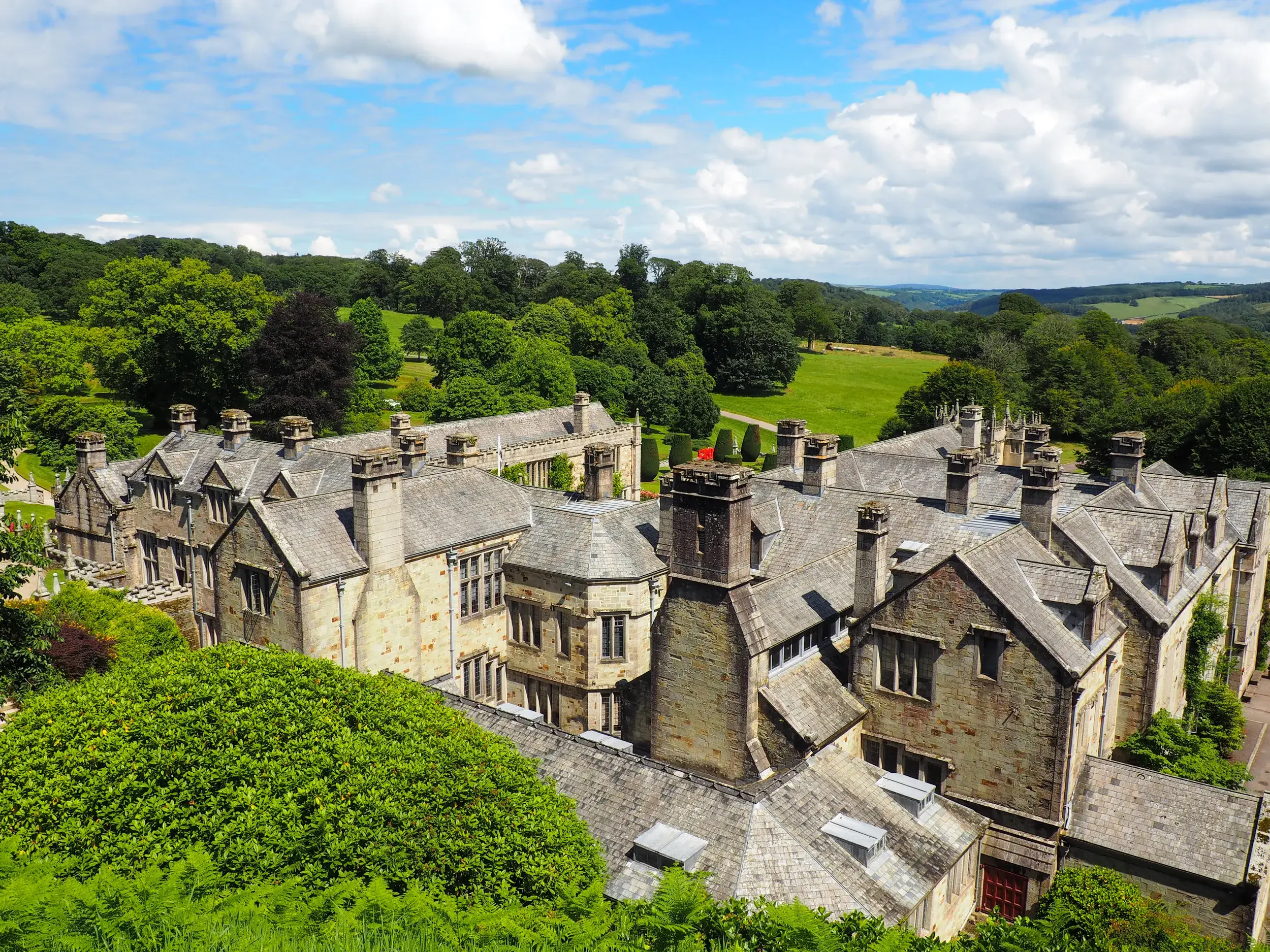 Blick von oben auf das viktorianische Herrenhaus Lanhydrock, umgeben von Gärten und der grünen Hügellandschaft Cornwalls.