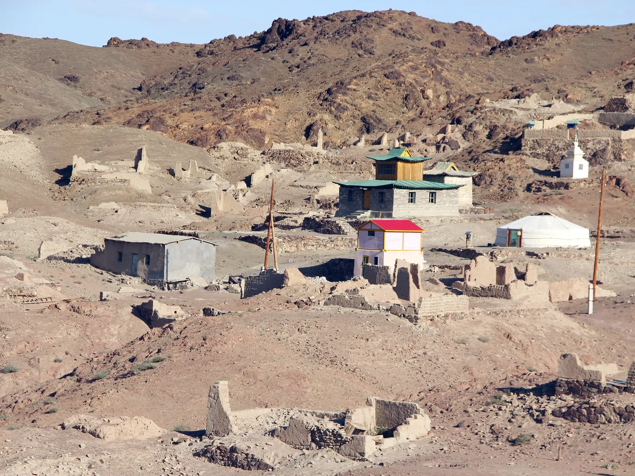 Das teilweise wiederaufgebaute Kloster Ongi in der Mongolei mit einem Tempel, einer Jurte und Ruinen in karger Hügellandschaft.