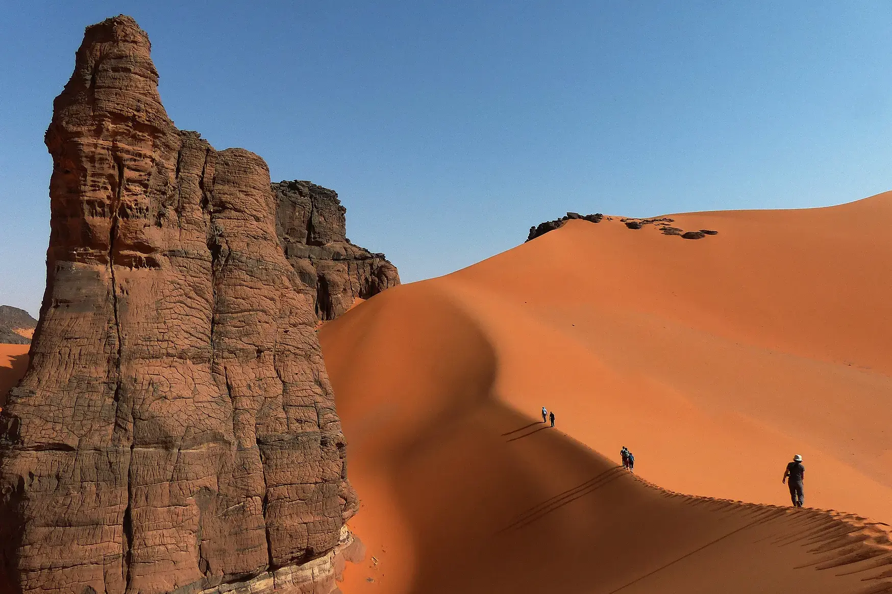 Wanderer auf dem Grat einer gewaltigen Sanddüne bei einer Trekkingreise durch die Felswüste des Tadrart in Algerien.