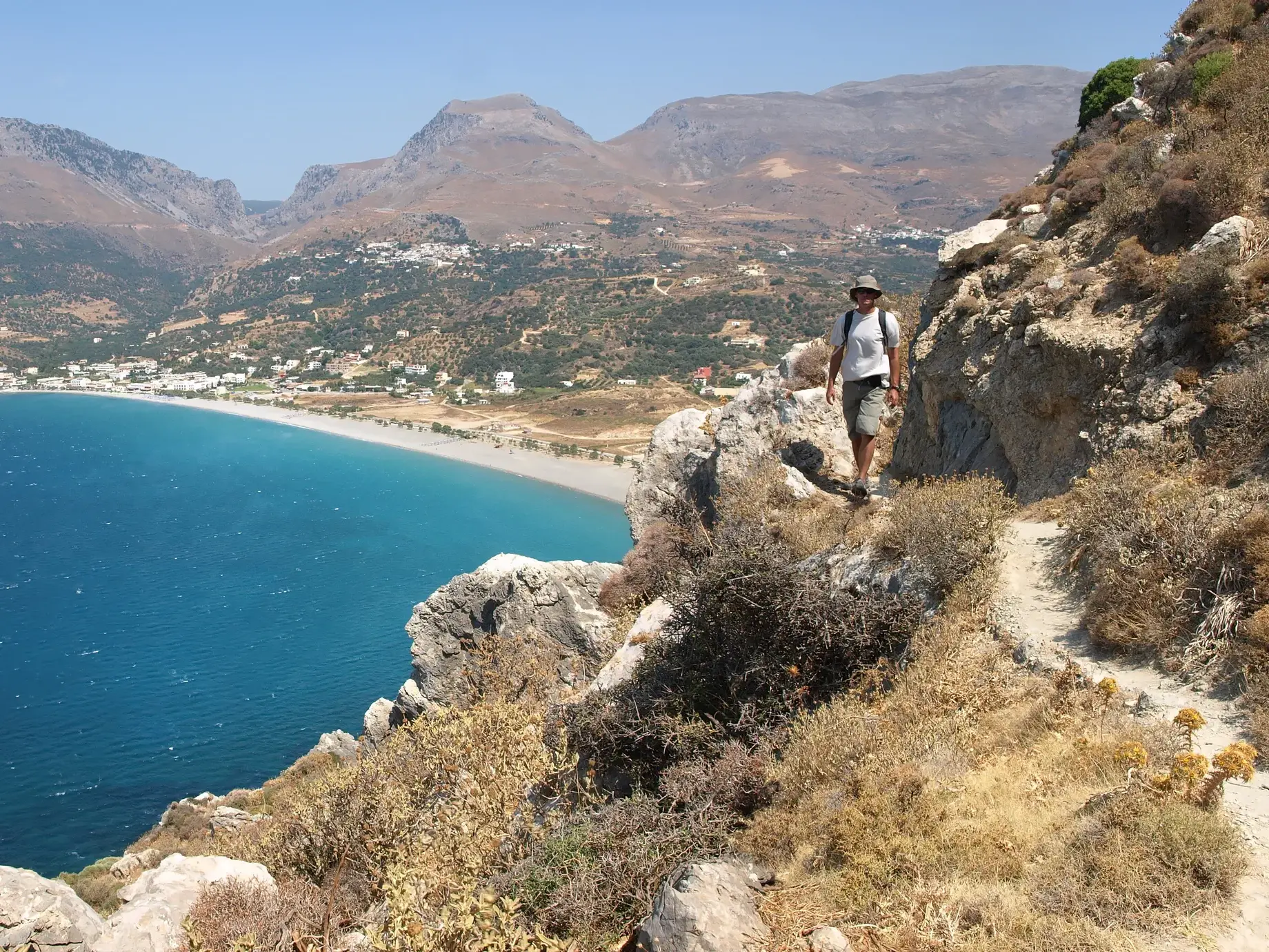 Wanderer auf einem Küstenpfad des Fernwanderwegs E4 mit Panoramablick auf eine Bucht an Kretas Südküste.
