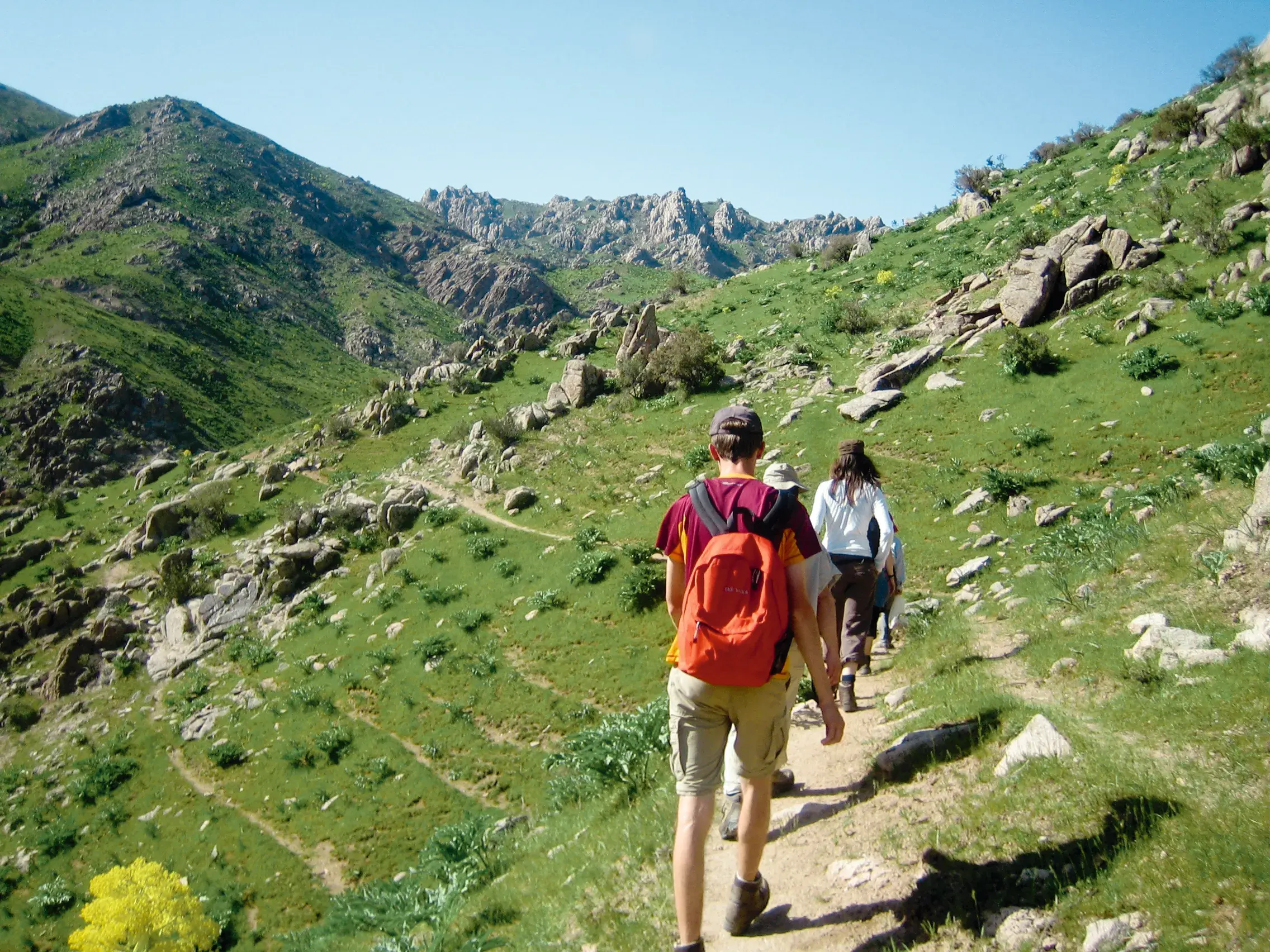 Teilnehmer einer Kleingruppenreise wandern auf einem Pfad durch die grünen, felsigen Nuratauberge in Usbekistan.