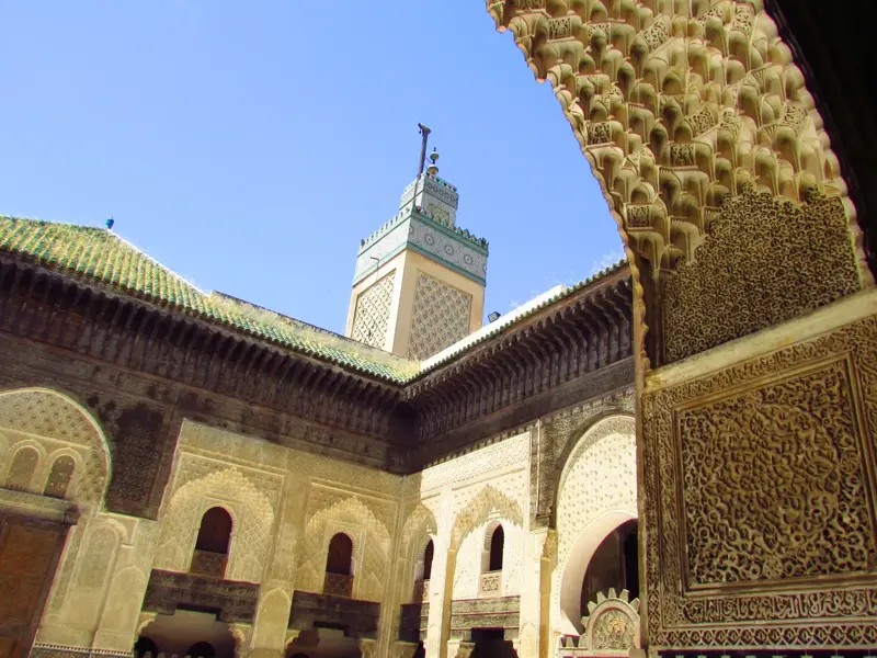 Sonniger Innenhof der Koranschule Medersa Ben Youssef in Marrakech mit kunstvollen Stuckarbeiten und dem grünen Minarett.