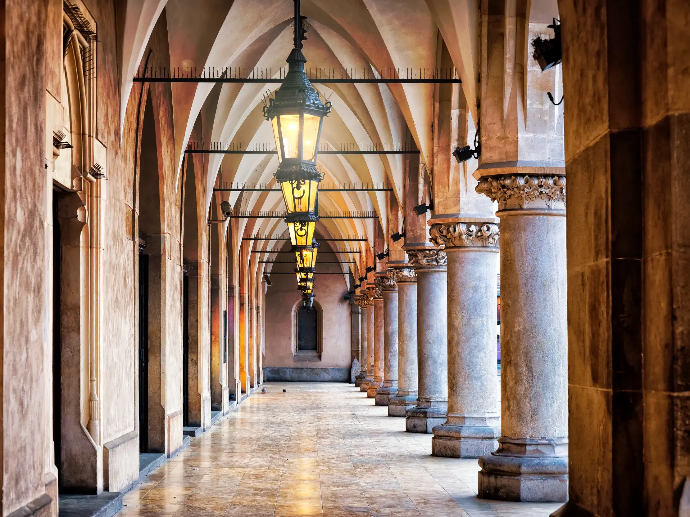 Die historischen Arkaden der Tuchhallen in der Altstadt von Krakau, beleuchtet von einer Reihe kunstvoller Laternen.
