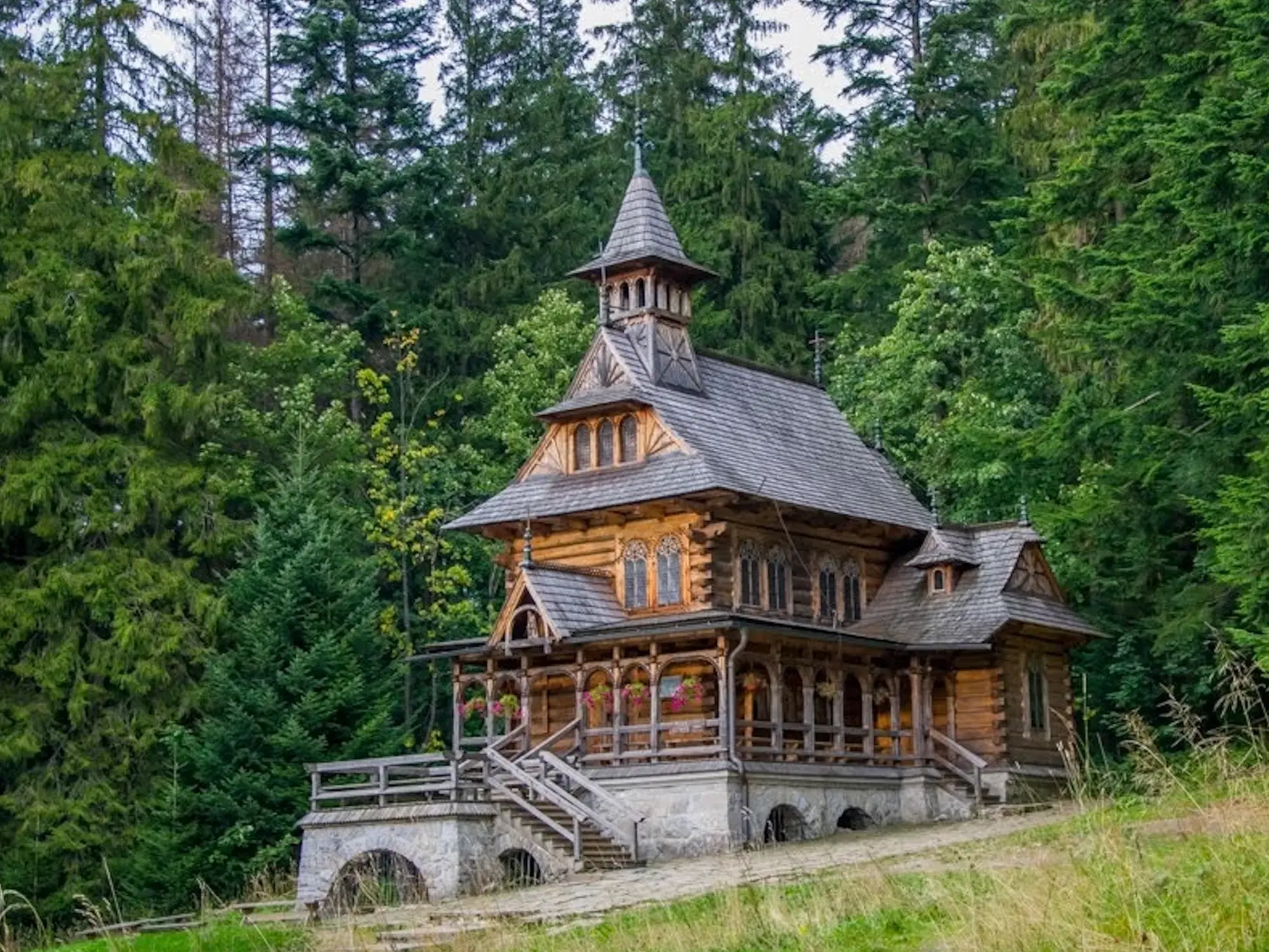 Die kunstvoll verzierte Bergkirche Javorina aus Holz an einem Hang, umgeben von dichten Wäldern der Hohen Tatra auf einer Wanderreise.