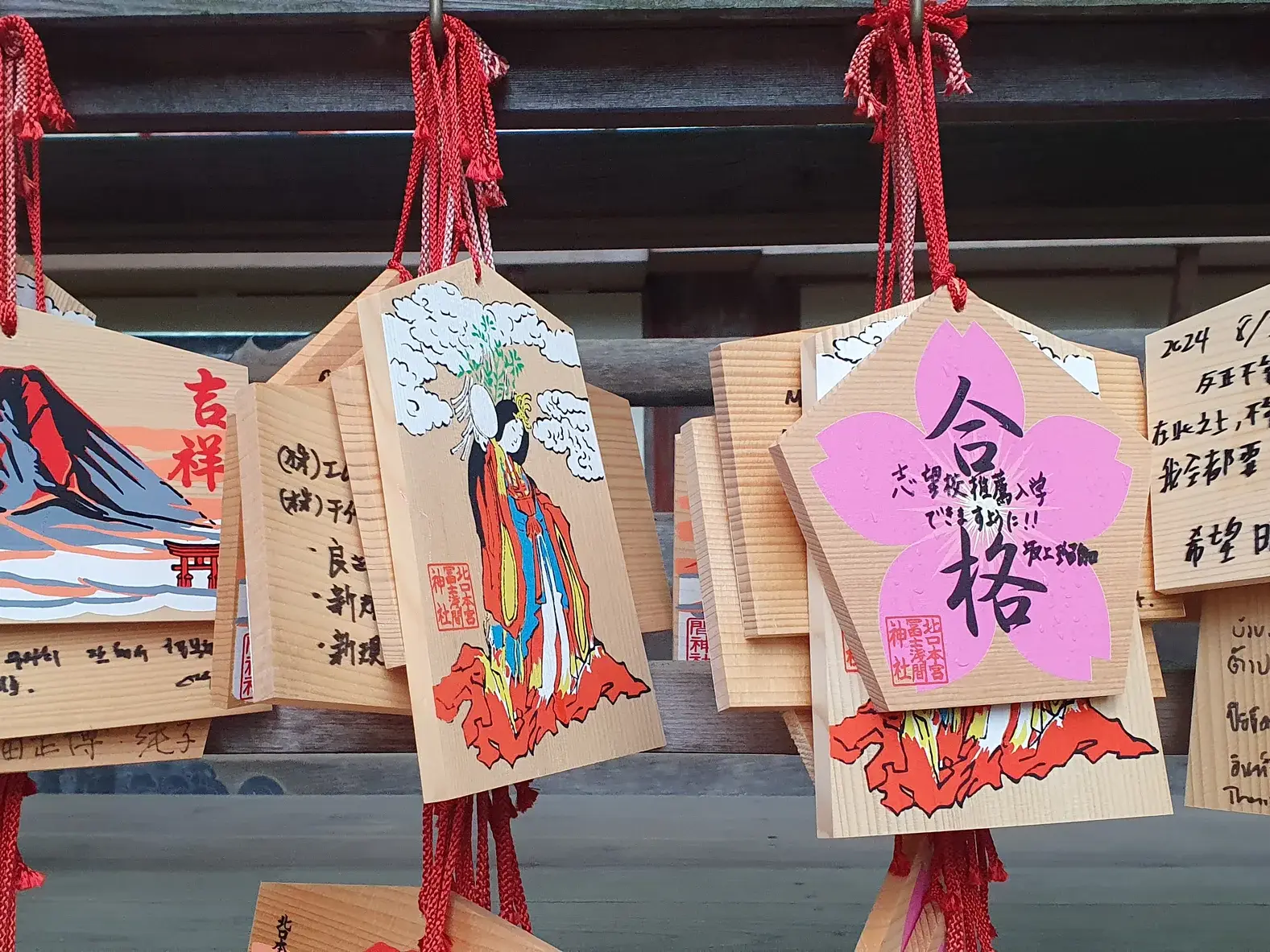 Nahaufnahme traditioneller Ema-Wunschtafeln mit Gebeten, bemalt mit dem Fuji und Kirschblüten, an einem japanischen Schrein.