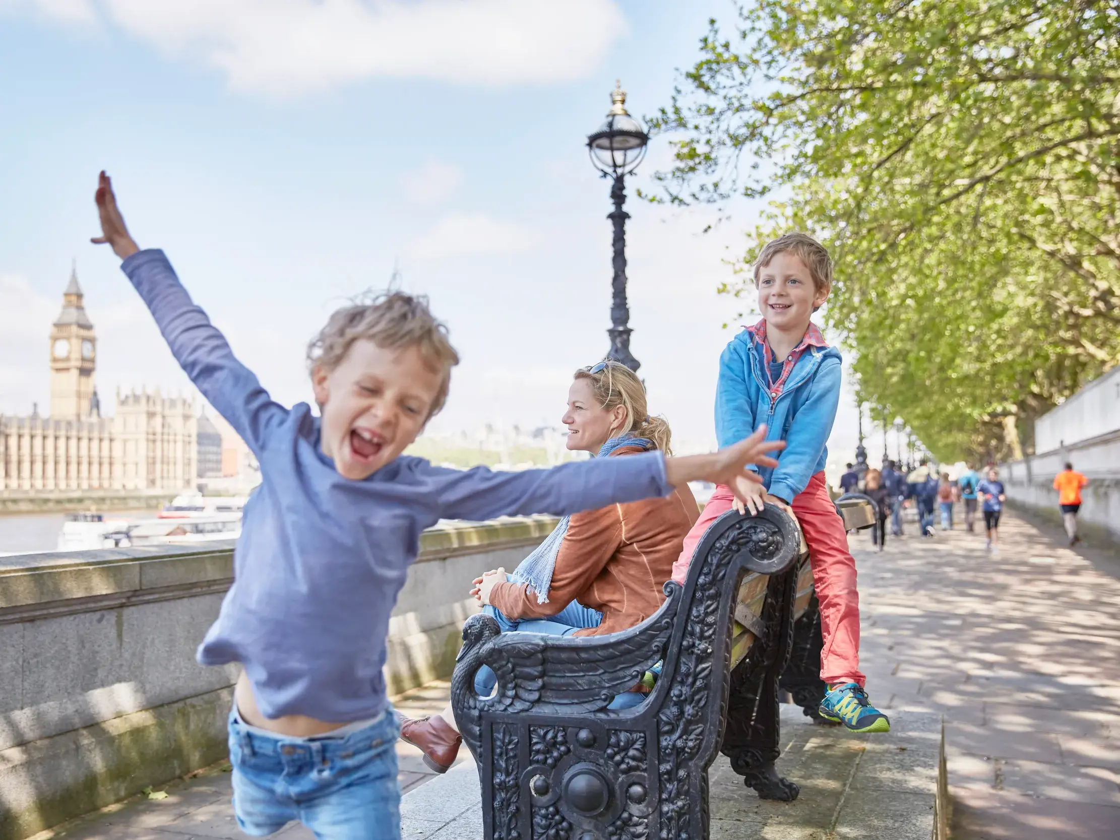 Gegenüber von Parlament und Big Ben sitzt eine Frau mit zwei spielenden Kindern am Themseufer.