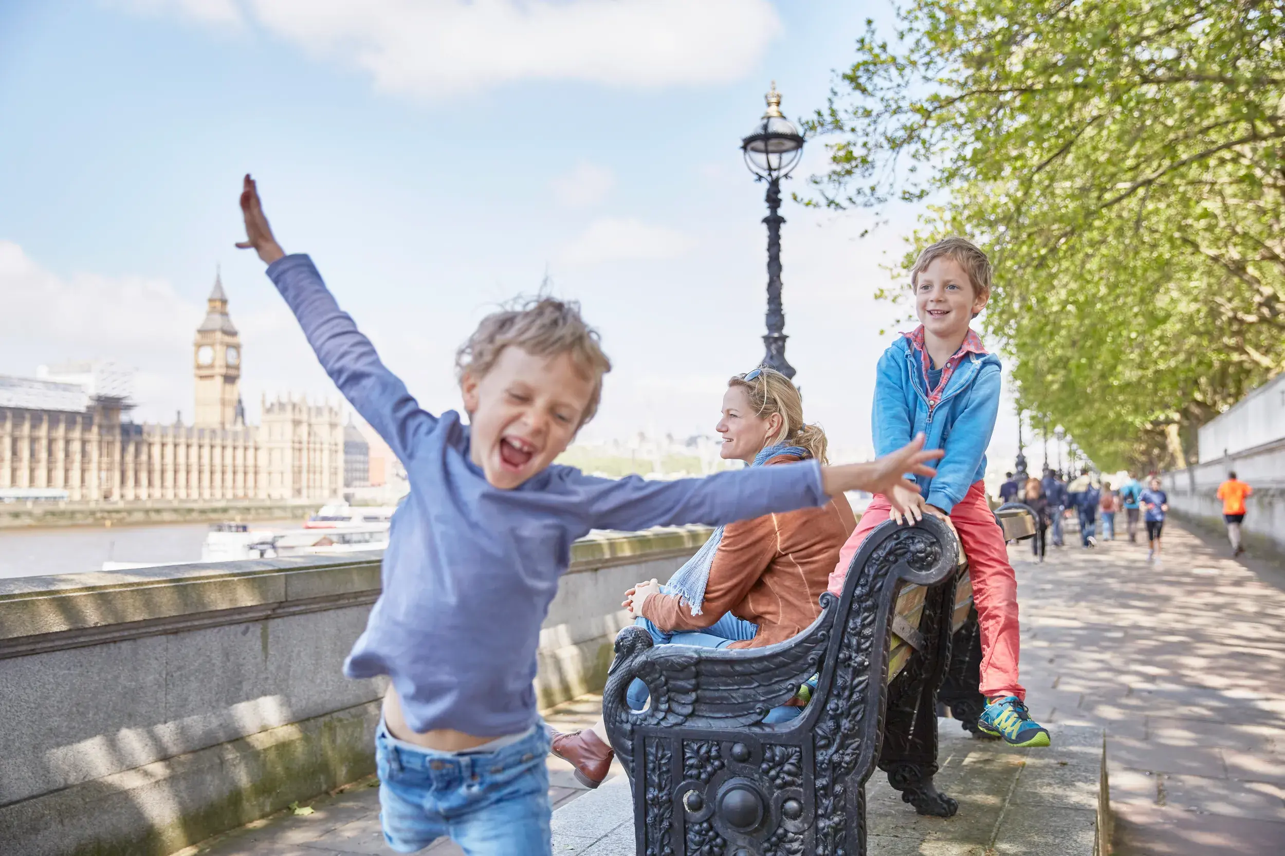 Gegenüber von Parlament und Big Ben sitzt eine Frau mit zwei spielenden Kindern am Themseufer.